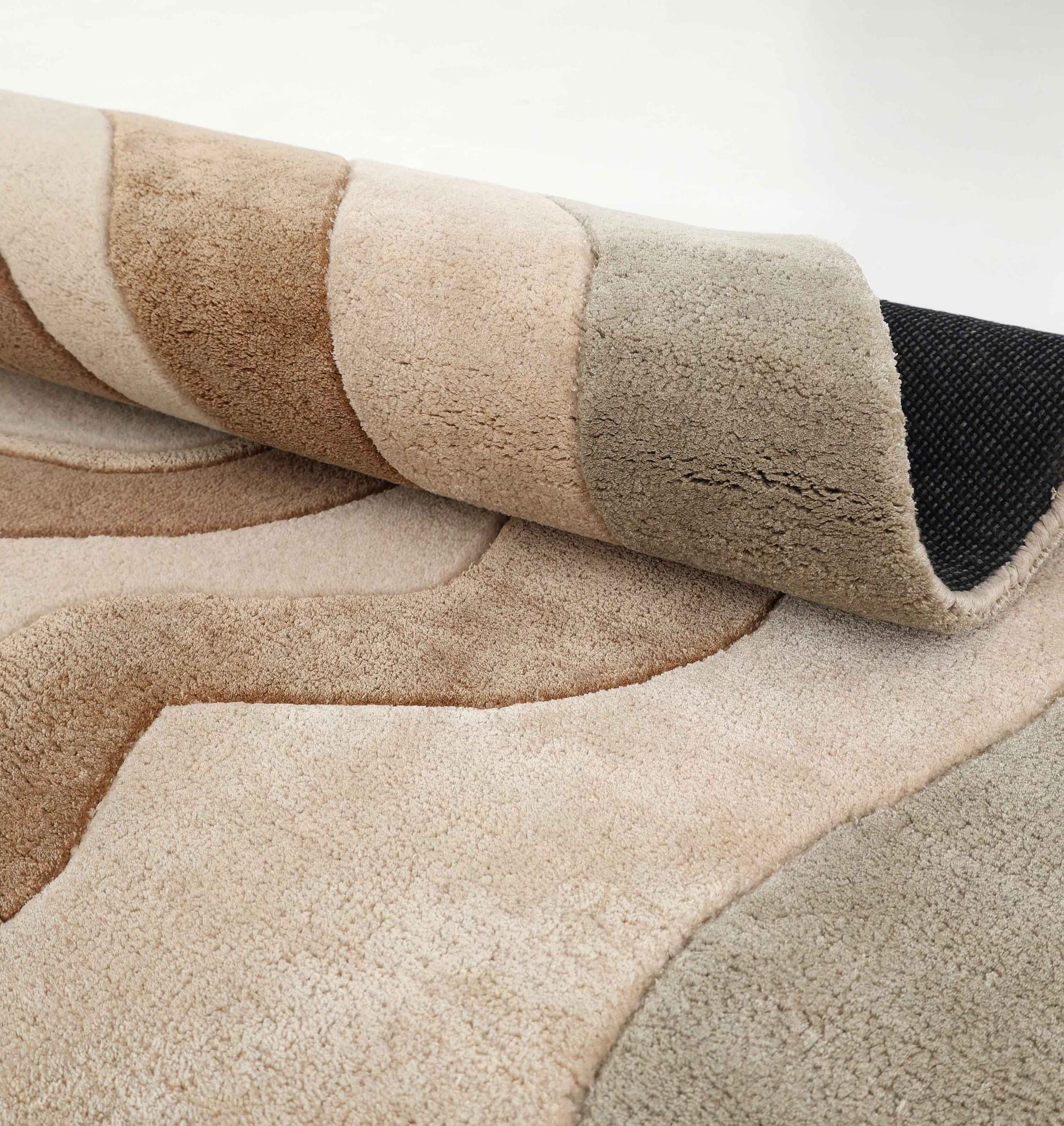 A close-up of the RAMSHA HOME Designer Freeform Handmade Rug HTWV-200, featuring plush, abstract wavy ovals in beige, brown, and gray with a black textured backing visible at a rolled corner.