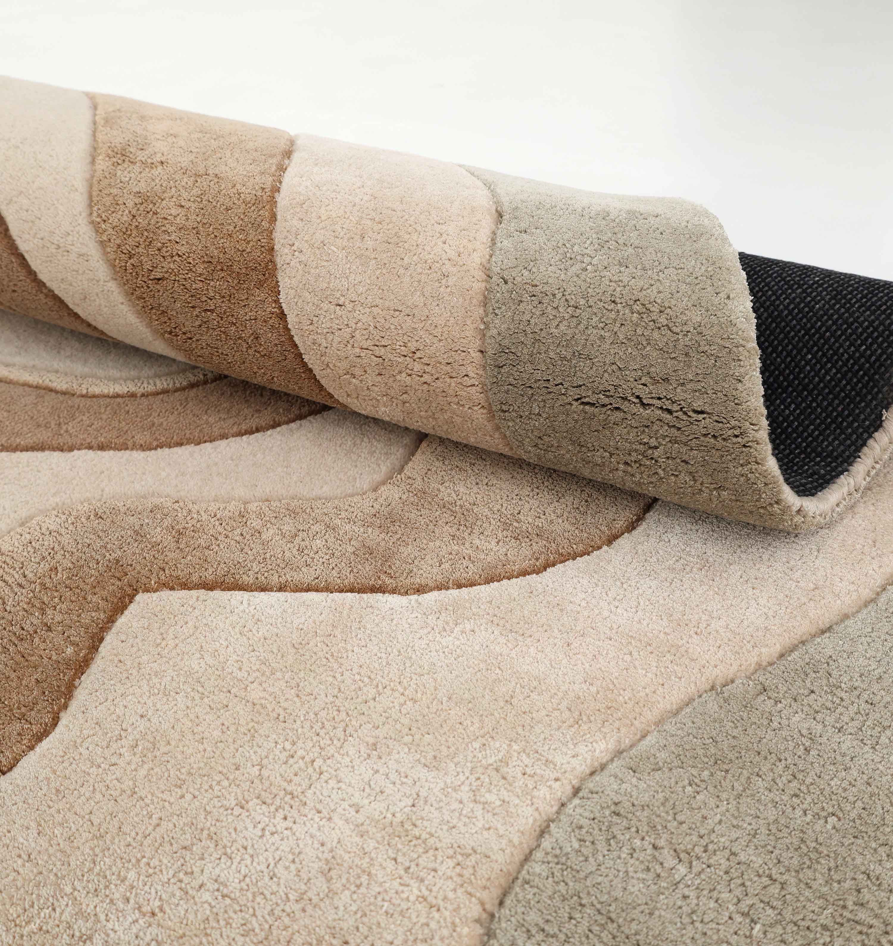 A close-up of the RAMSHA HOME Designer Freeform Handmade Rug HTWV-200, featuring plush, abstract wavy ovals in beige, brown, and gray with a black textured backing visible at a rolled corner.