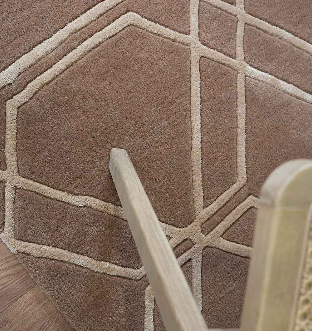 A close-up of the RAMSHA HOME Stunning Multi Color Hand-Tufted Rug - HTWV 21 (200x300cm), featuring a brown base with a beige geometric hexagon pattern, partially covered by a wooden chair leg.