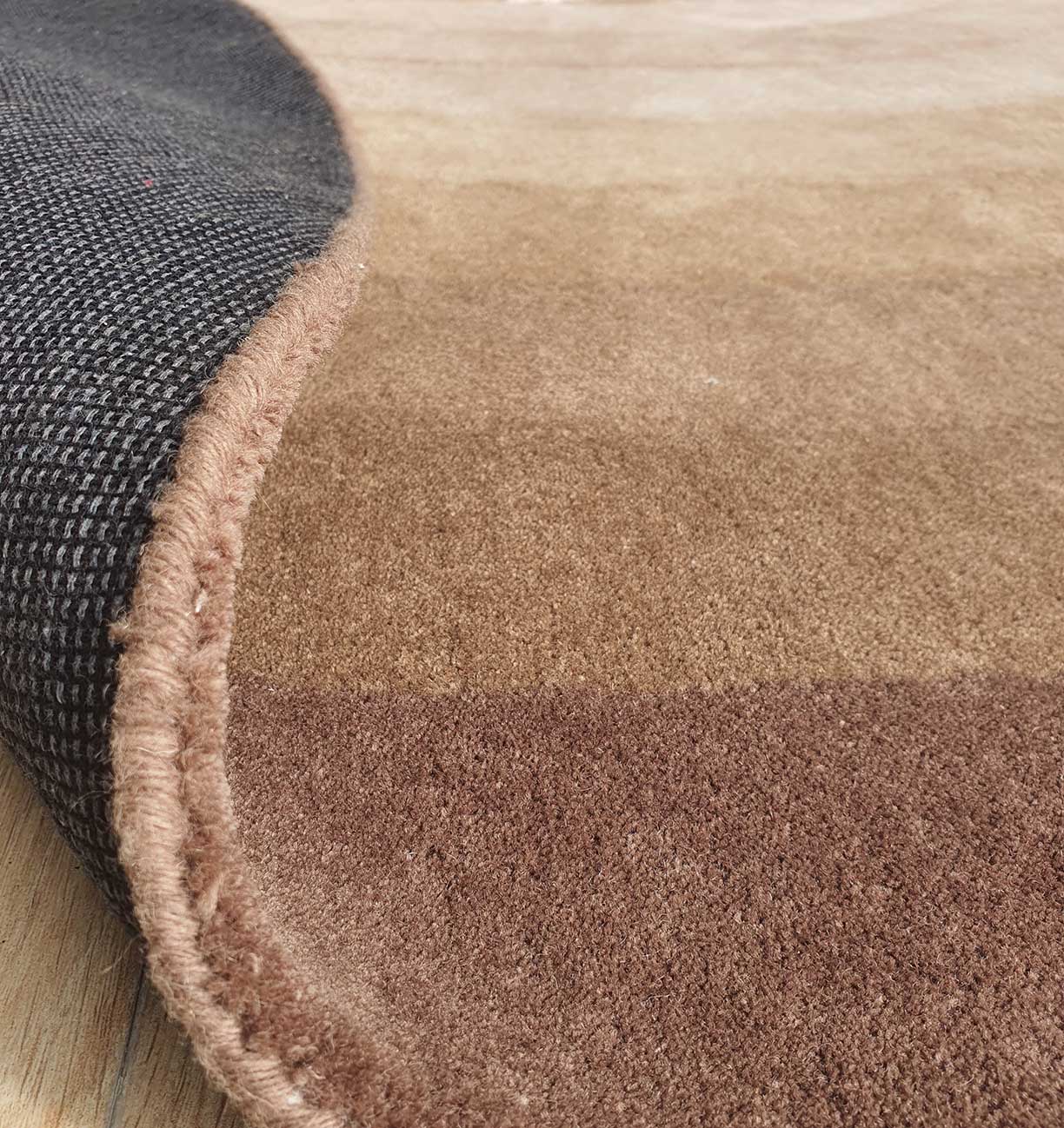 Close-up of the RAMSHA HOME Luxurious Wool & Cotton Handmade Rug - HTWV 55 (300cm) in brown, showing its dark textured underside with a flipped corner, handtufted and laid on a wooden floor.