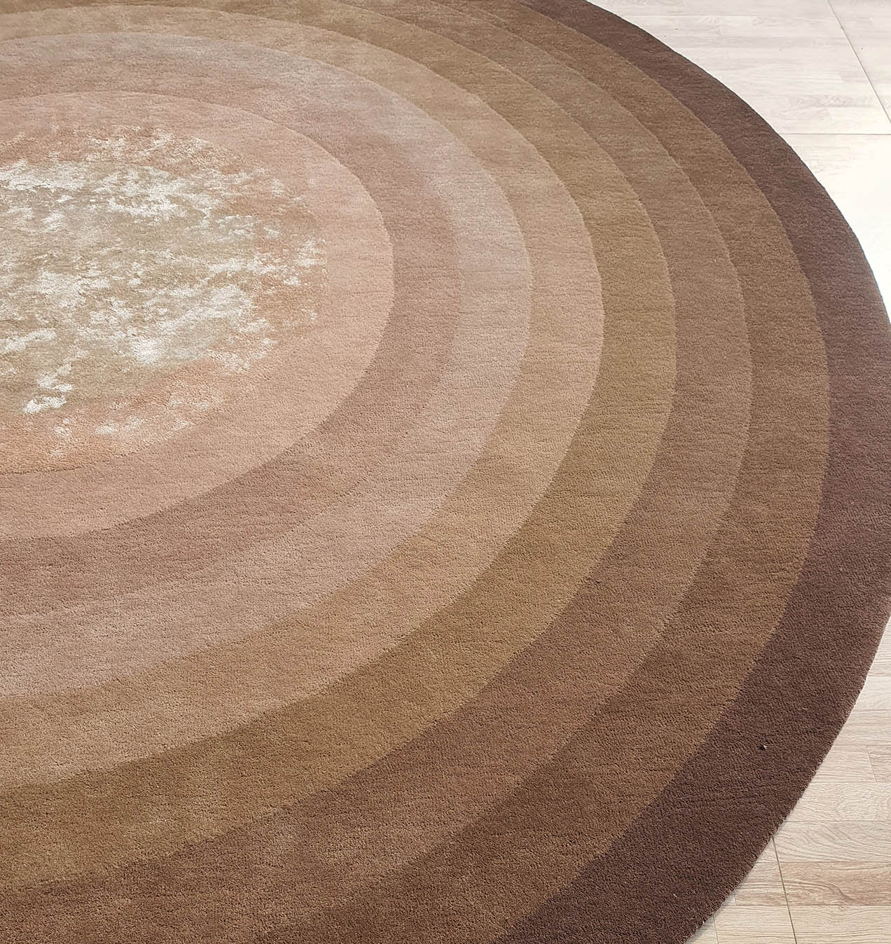 The RAMSHA HOME Luxurious Wool & Cotton Handmade Rug - HTWV 55 (300cm) is a handtufted, round rug with concentric rings in brown and beige shades and a subtly textured center, shown on a light wood floor.