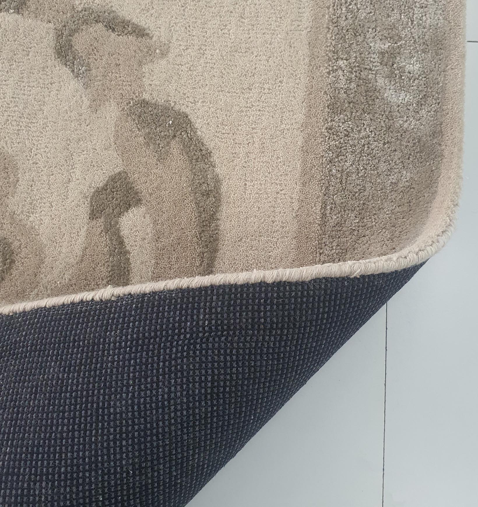 A corner of the RAMSHA HOME Amazing Multi Color Modern Floor Rug - HTWV 57 (300x400cm) is flipped, showing its dark, textured underside on a light tiled floor.