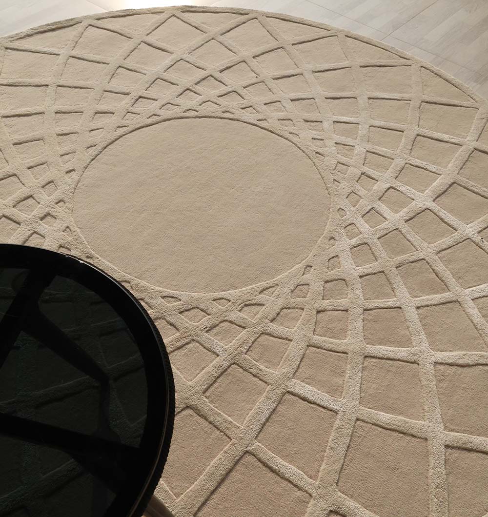 The RAMSHA HOME Handmade Round Area Rug - HTWV 61 (200 cm), in beige wool-viscose with an intricate geometric pattern, is partially covered by a black glass-topped table in the lower left corner.