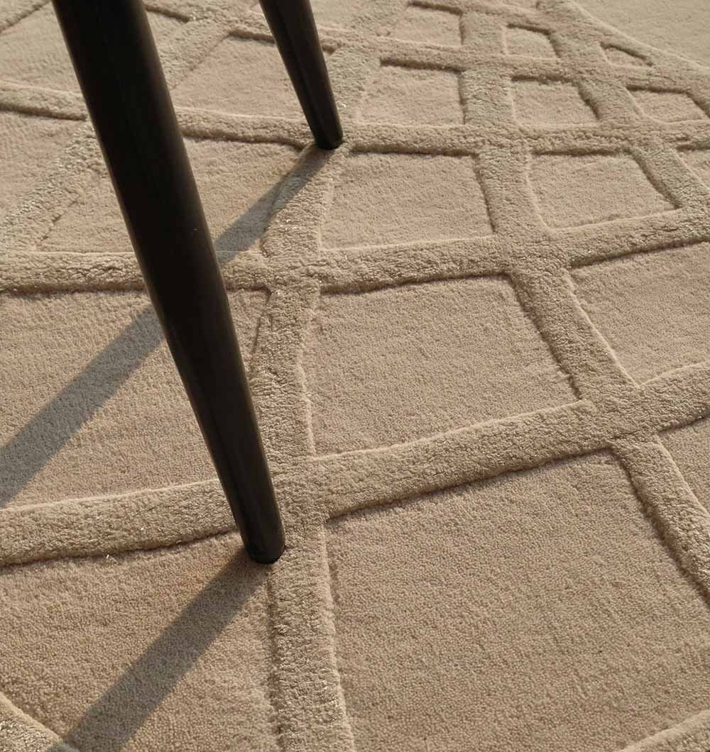 The image features the Handmade Round Area Rug - HTWV 61 (200 Cm) by RAMSHA HOME, a beige wool-viscose rug with a raised grid pattern of intersecting lines forming squares, alongside two partially visible dark chair legs.
