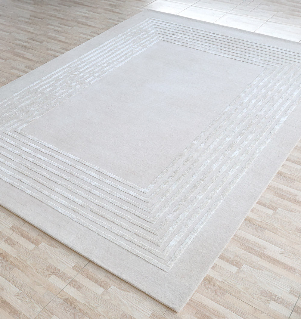 The RAMSHA HOME Hand-Tufted Carpet For Home And Office HTWV-70, a large rectangular rug in light beige with a subtle geometric border, is placed on a light wood floor in a bright, naturally lit room.