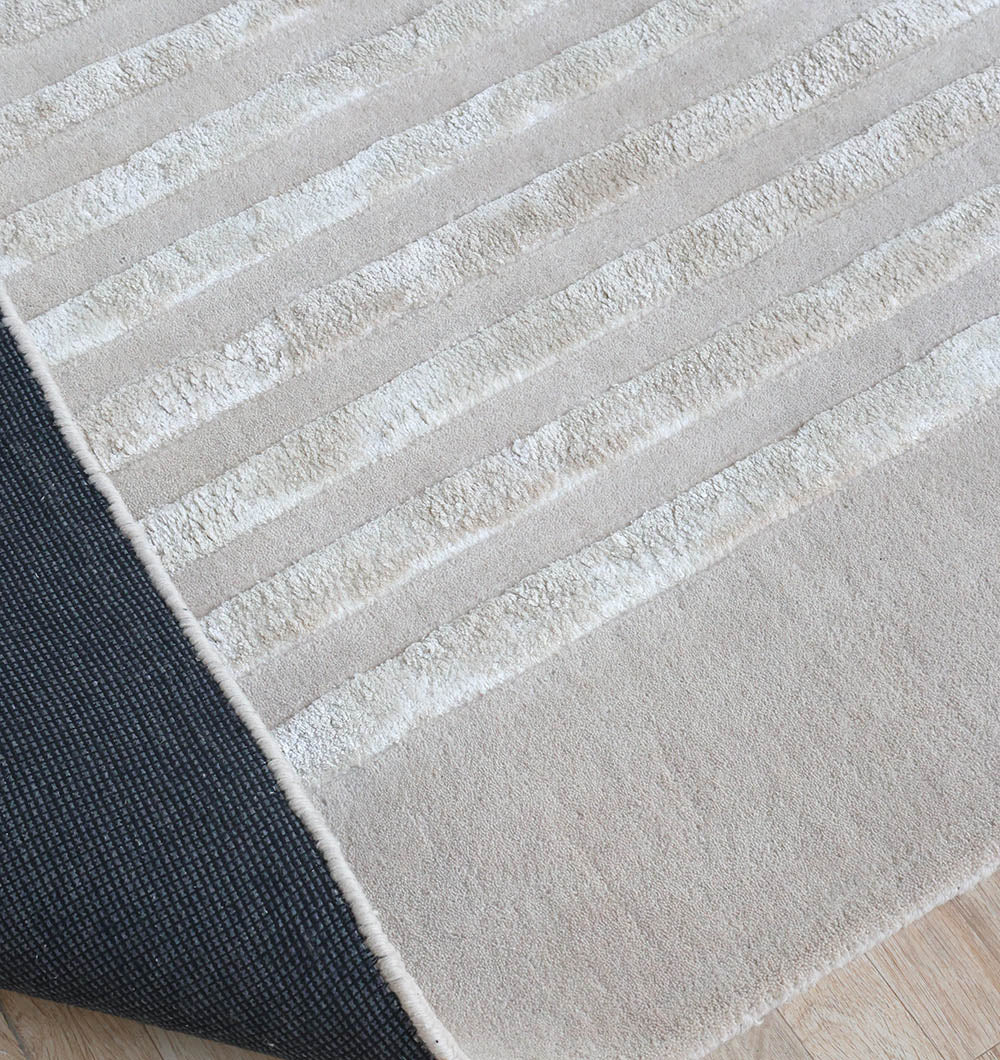 The RAMSHA HOME Hand-Tufted Carpet For Home And Office HTWV-70, featuring beige textured horizontal stripes, is shown partially folded to display its dark underside on a light wood floor.