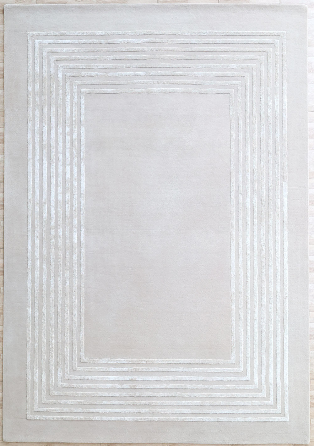 The RAMSHA HOME Hand-Tufted Carpet For Home And Office HTWV-70 is a contemporary beige wool rug with thin white lines forming concentric rectangles near the border, perfect for modern minimalist interiors.