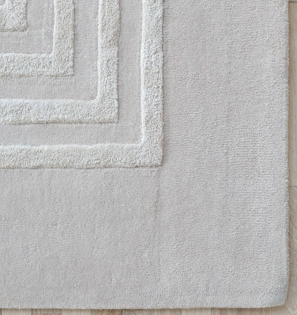 Close-up of the RAMSHA HOME Hand-Tufted Carpet For Home And Office HTWV-70, a beige rectangular rug with textured concentric square patterns in one corner, shown on a light wooden floor.