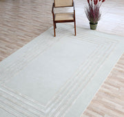 The Hand-Tufted Carpet For Home And Office HTWV-70 by RAMSHA HOME, featuring a geometric border, is laid on a tiled floor with a wooden chair and potted plant placed on this contemporary wool rug.