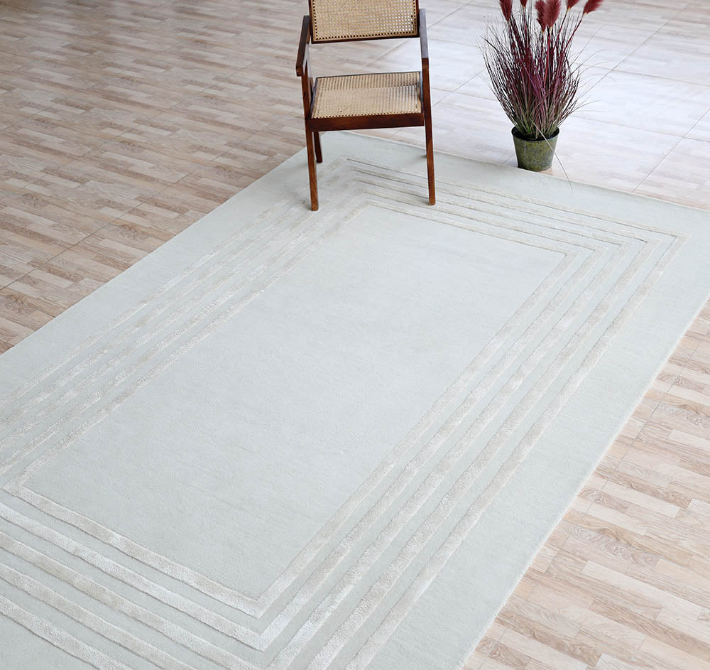 The Hand-Tufted Carpet For Home And Office HTWV-70 by RAMSHA HOME, featuring a geometric border, is laid on a tiled floor with a wooden chair and potted plant placed on this contemporary wool rug.