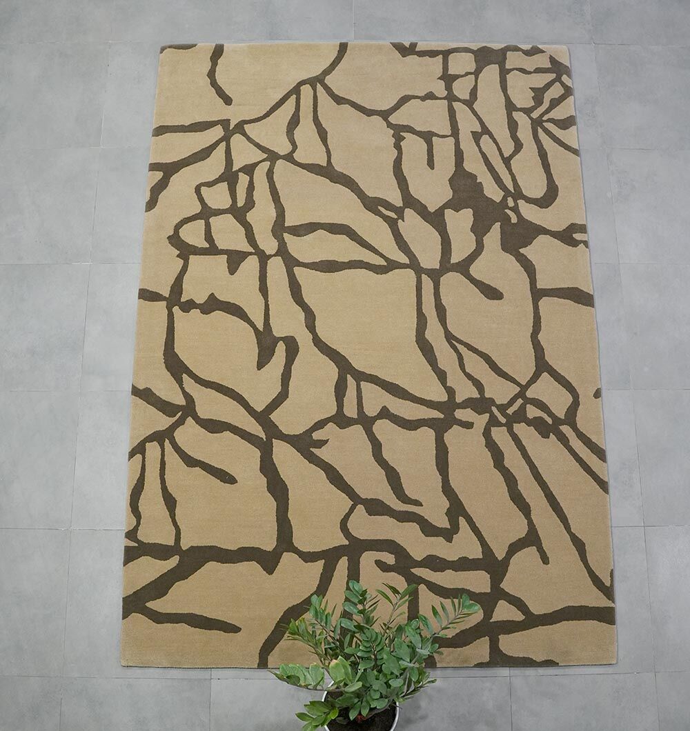 The RAMSHA HOME Stunning Multi Color Fluffy Wool Handmade Rug - HTW 21 (202x292cm) features a modern abstract design on beige, with dark brown branch-like patterns and rests on light gray tiles, accented by a green potted plant nearby.