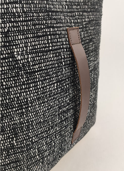 Close-up of the RAMSHA HOME Black Cotton Pouf With Leather Handle PF-046, showcasing its textured black and white woven fabric and a vertically stitched brown leather handle against a plain light background.