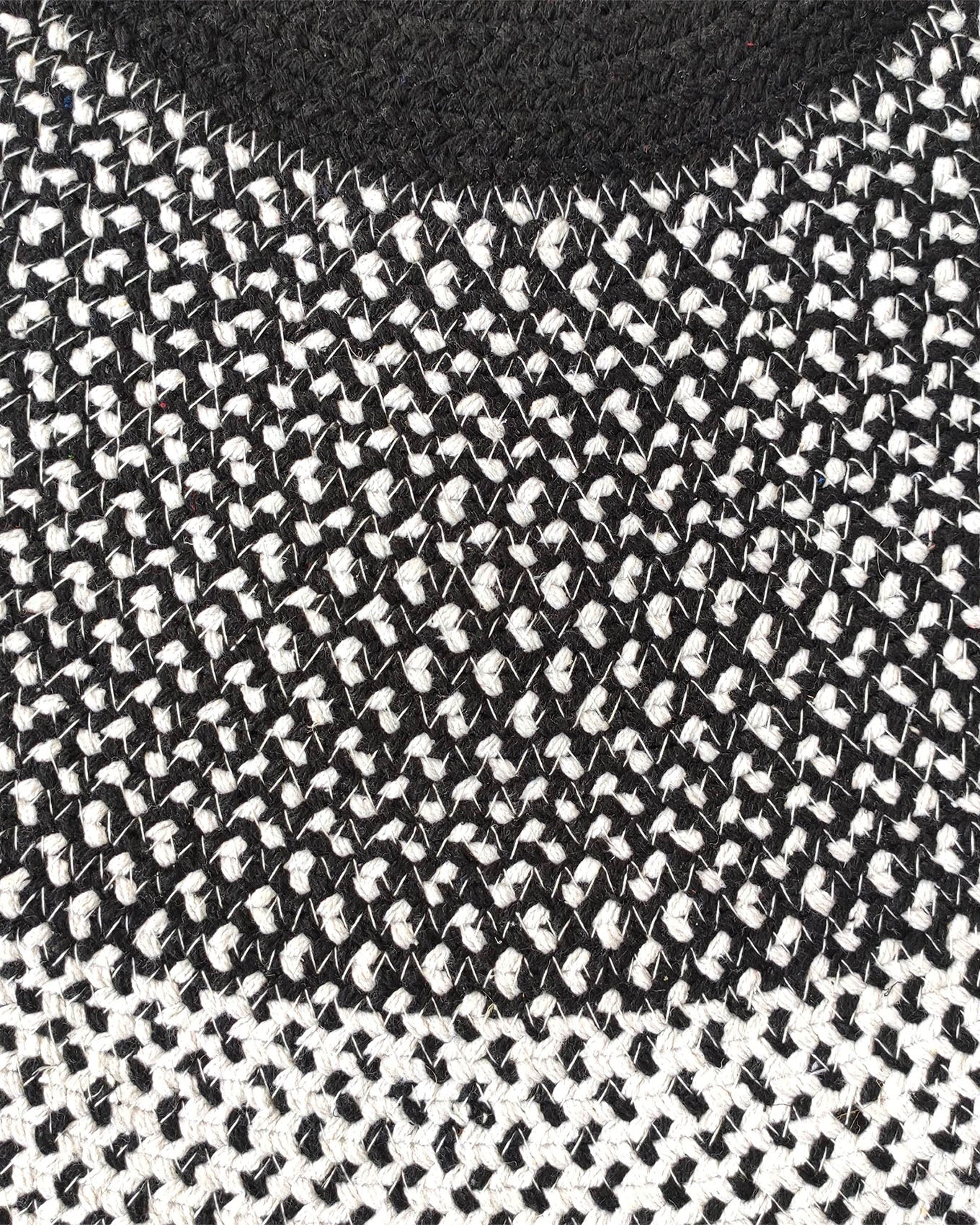 Close-up of a black and white knitted fabric with an interwoven pattern, resembling the RAMSHA HOME Black & White Color Round Braided Rug - BR 010; its top section is solid black, blending into a mix of black and white threads.