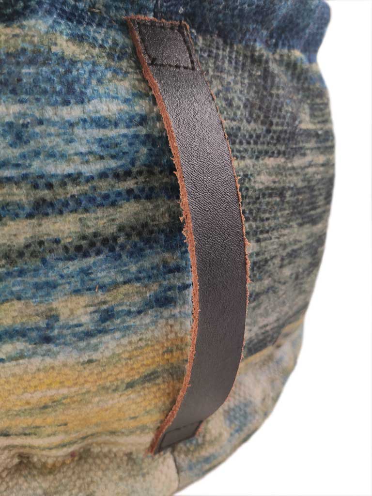 Close-up of the RAMSHA HOME Printed Multi Color Pouf With Leather Handle, showing its textured fabric in blue, yellow, and gray hues with a dark brown stitched leather handle.