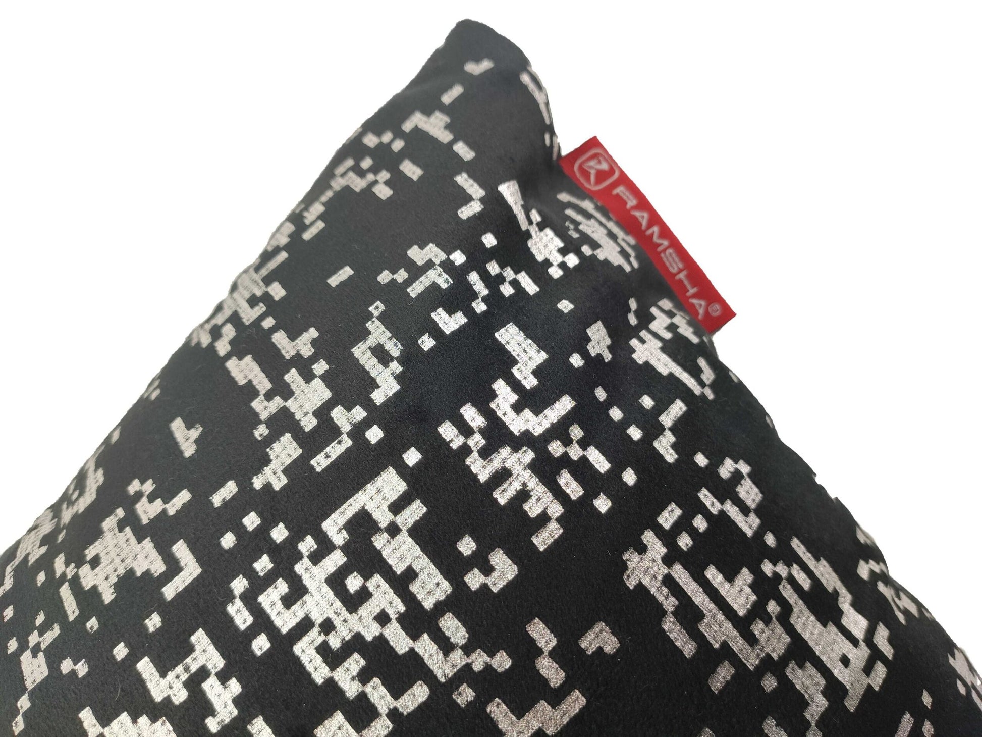 A close-up of the Decorative Black Color Cushion CS-095 by RAMSHA HOME, featuring a silver pixelated pattern and a red fabric tag with the brand name attached to one corner.
