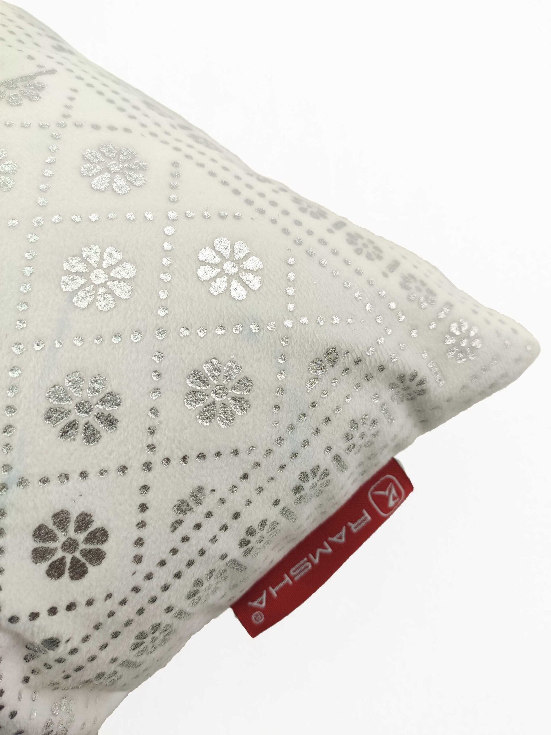 A close-up of the Home Decor Polyester Cushion by RAMSHA HOME, cream-colored with silver floral and diamond patterns, features a red RAMSHA tag on the side, making it a stylish accent for any space against a plain white background.