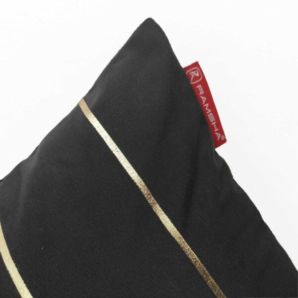 Close-up of the RAMSHA HOME 100% Polyester Cushion Cover CS-099 in black, featuring two diagonal gold stripes and a red RAMSHA fabric tag on the corner; wrinkle-resistant and durable cover displayed against a white background.