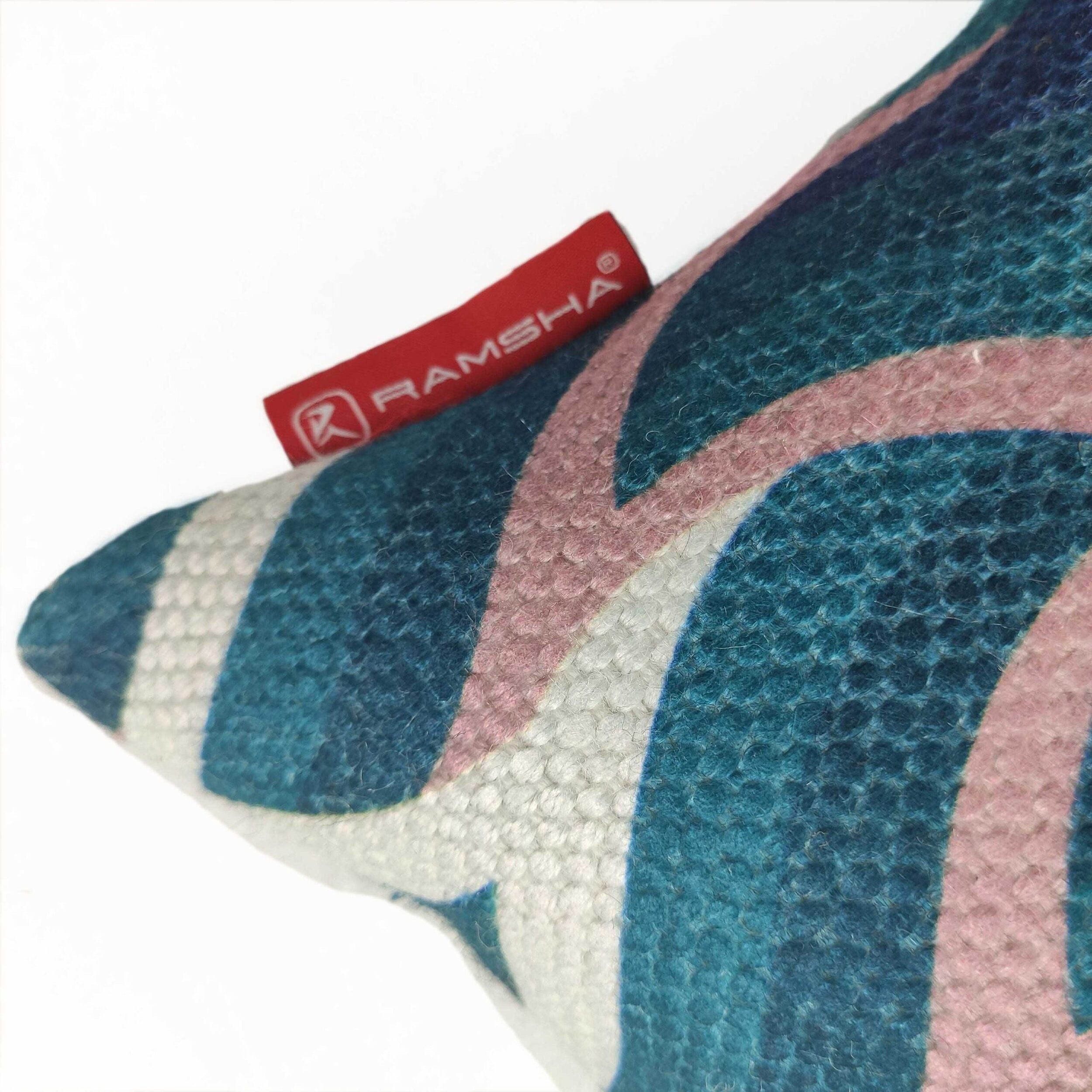 A close-up of the Cushion Cover Multi Color CS-069 by RAMSHA HOME shows its textured polyester fabric with blue, pink, and beige swirl patterns. A red tag featuring the white RAMSHA HOME logo is attached to the edge.