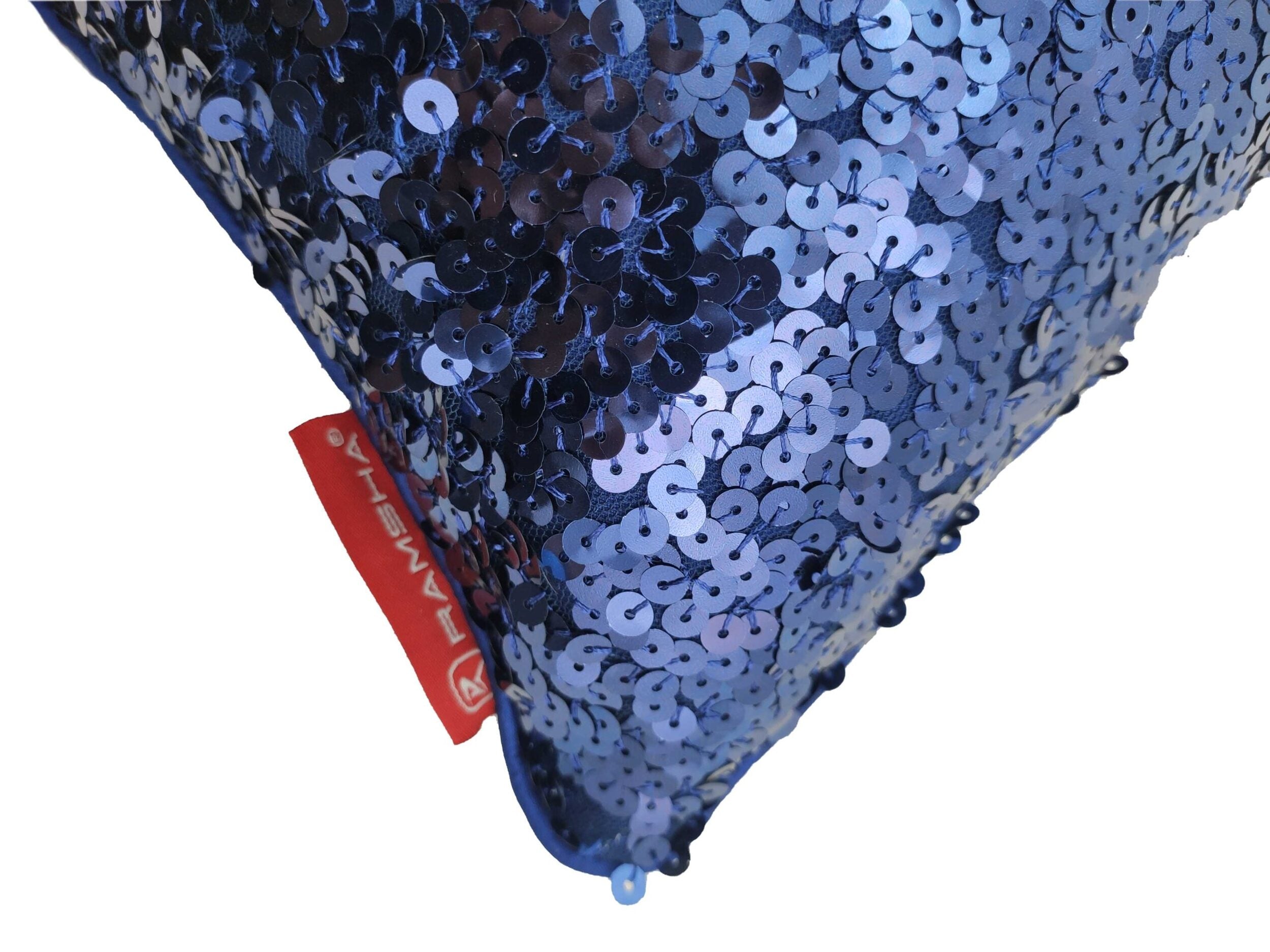 Close-up of the corner of a RAMSHA HOME Home Decor Polyester Cushion With Filler, featuring blue sequins and a red fabric tag. The shiny surface adds sparkle and plush support to your space.