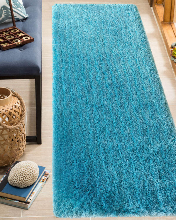 The Drawing Room Aqua Color Shaggy Rug - MPV 02 (60x180cm) by RAMSHA HOME stretches across a light-tiled floor beside a bench, decorative basket, and stacked books topped with a textured stone.