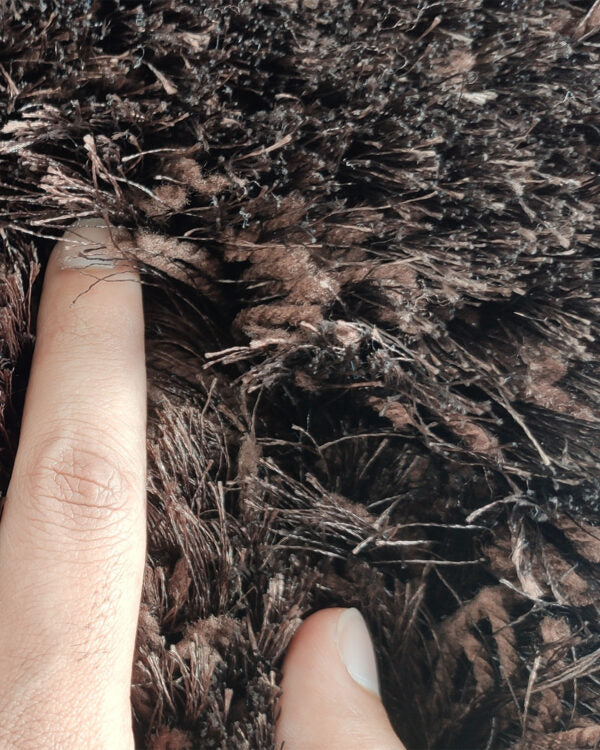 A close-up shows two fingers pressing into the thick, long strands of the RAMSHA HOME Fluffy Brown Color Dining Room Shaggy Rug - MPV 04 (60x180cm), highlighting its plush texture.
