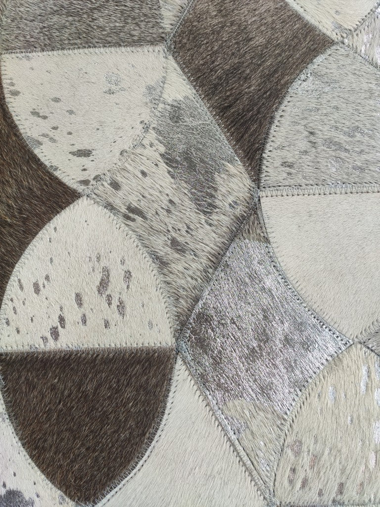 Close-up of the Delightful Modern Grey Color Leather Rug - LR 008 by RAMSHA HOME, showcasing patchwork cowhide in brown, cream, and gray tones with visible hair and stitched seams.