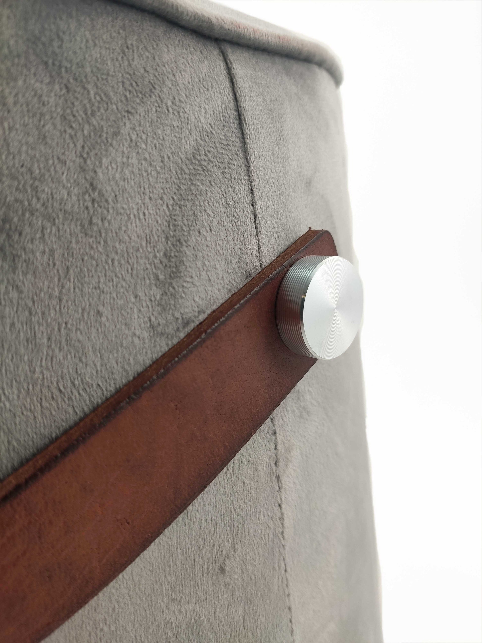 Close-up of the RAMSHA HOME Leather Pedestal Pouf With Leather Handle, featuring soft light gray fabric, a brown leather handle secured with a round silver knob, set against a clean white background highlighting its refined style.