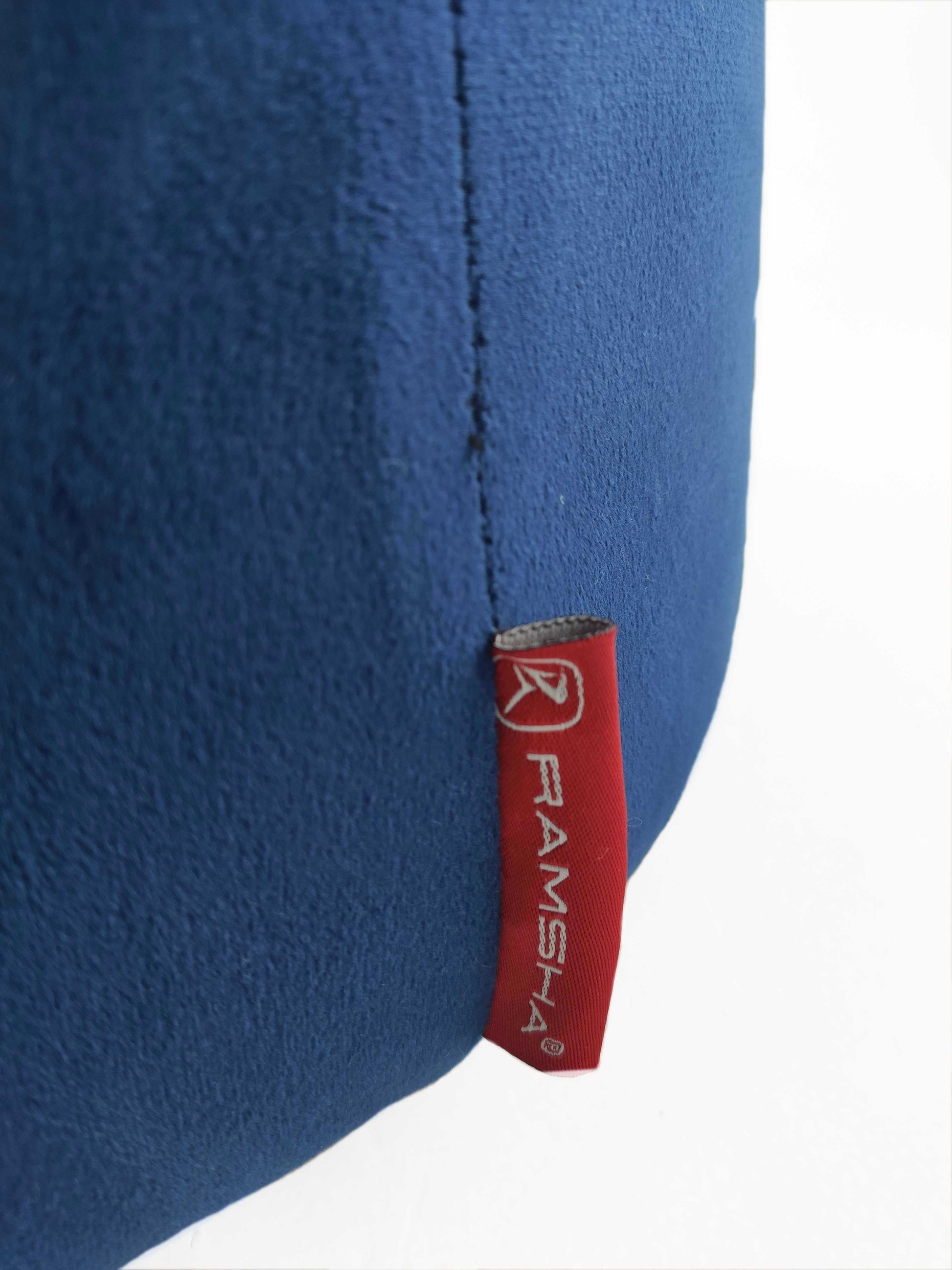 A close-up of a blue fabric surface with a red tag stitched into the seam, featuring the RAMSHA HOME logo in white, next to the Leather Pedestal Pouf With Leather Handle.