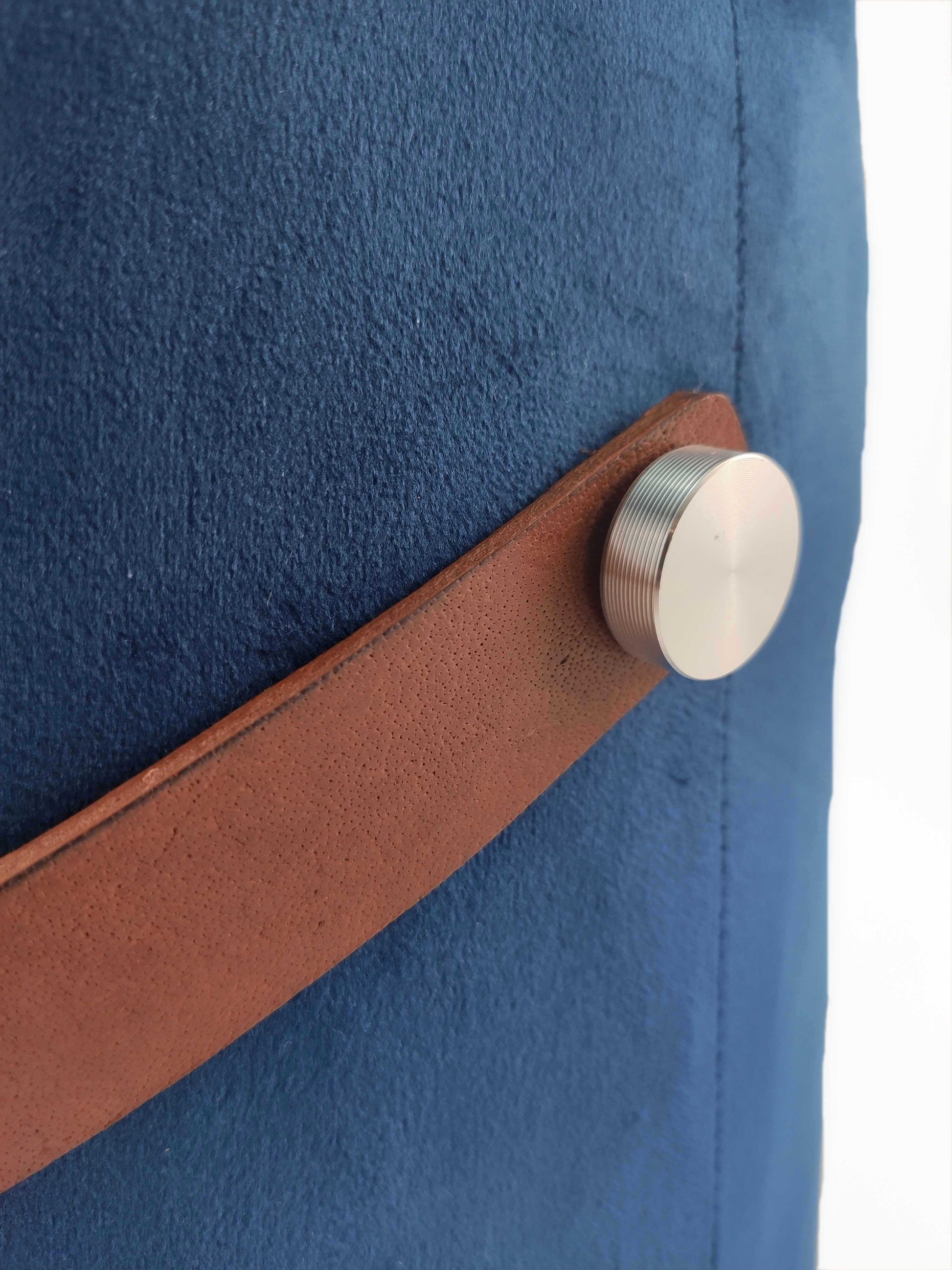 Close-up of the brown leather handle, secured by a round silver button, on the blue Leather Pedestal Pouf With Leather Handle by RAMSHA HOME. White background.