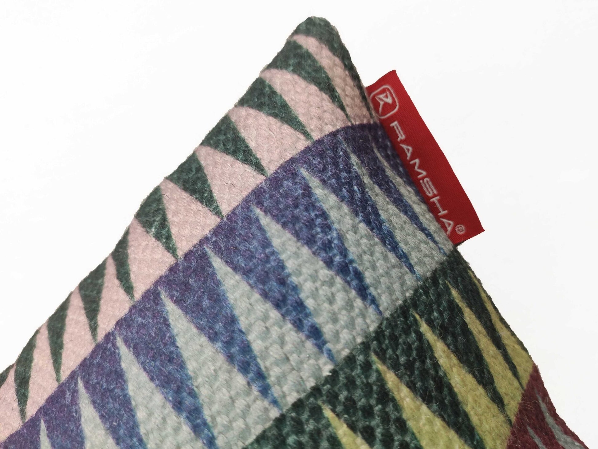A close-up of RAMSHA HOME’s Polyester Cushion Cover CS-068, featuring a wrinkle-resistant geometric pattern in purple, green, pink, and yellow. A red RAMSHA tag is attached at the upper corner. Ideal for indoor or outdoor use. Plain white background.
