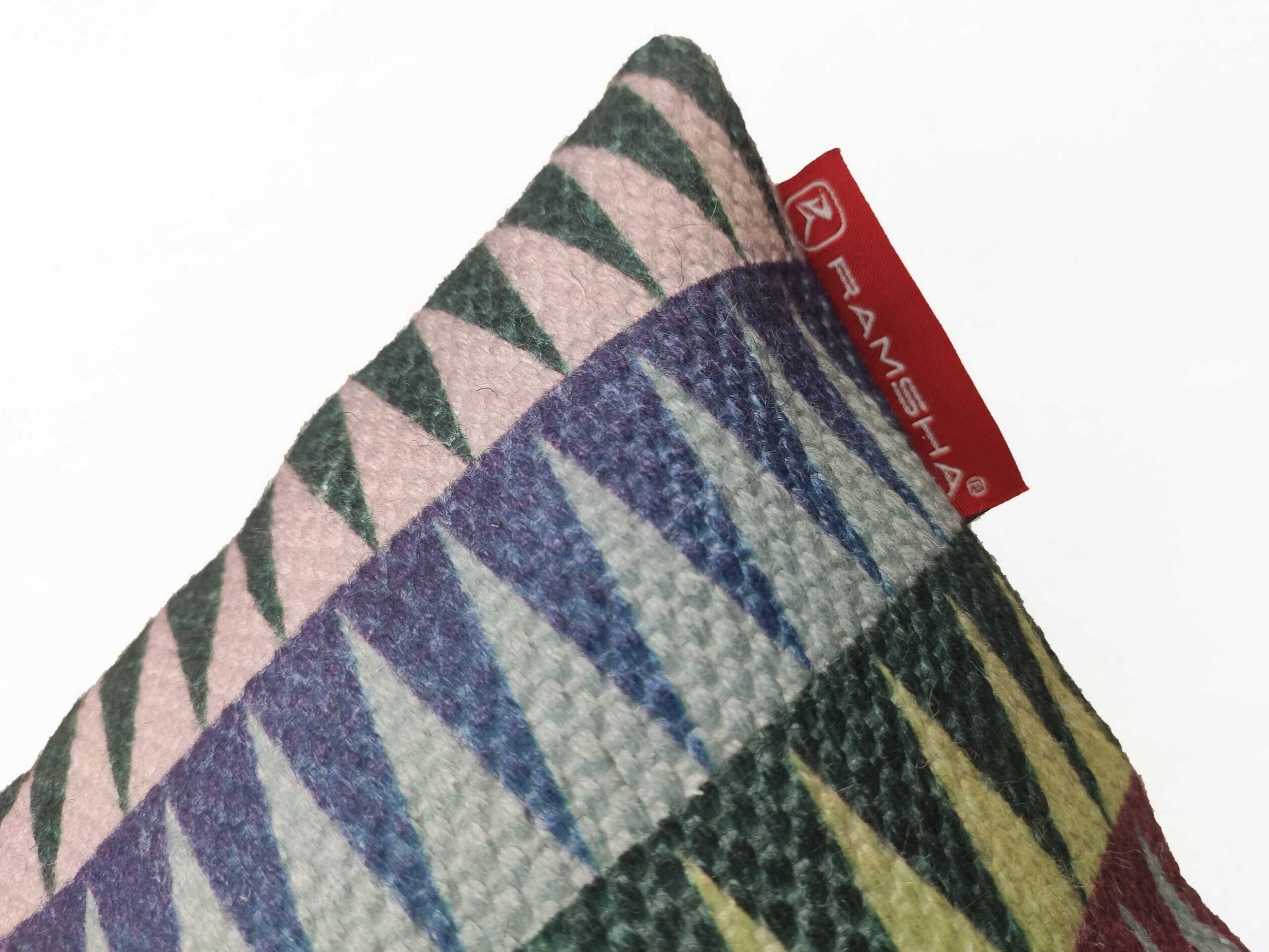 A close-up of RAMSHA HOME’s Polyester Cushion Cover CS-068, featuring a wrinkle-resistant geometric pattern in purple, green, pink, and yellow. A red RAMSHA tag is attached at the upper corner. Ideal for indoor or outdoor use. Plain white background.
