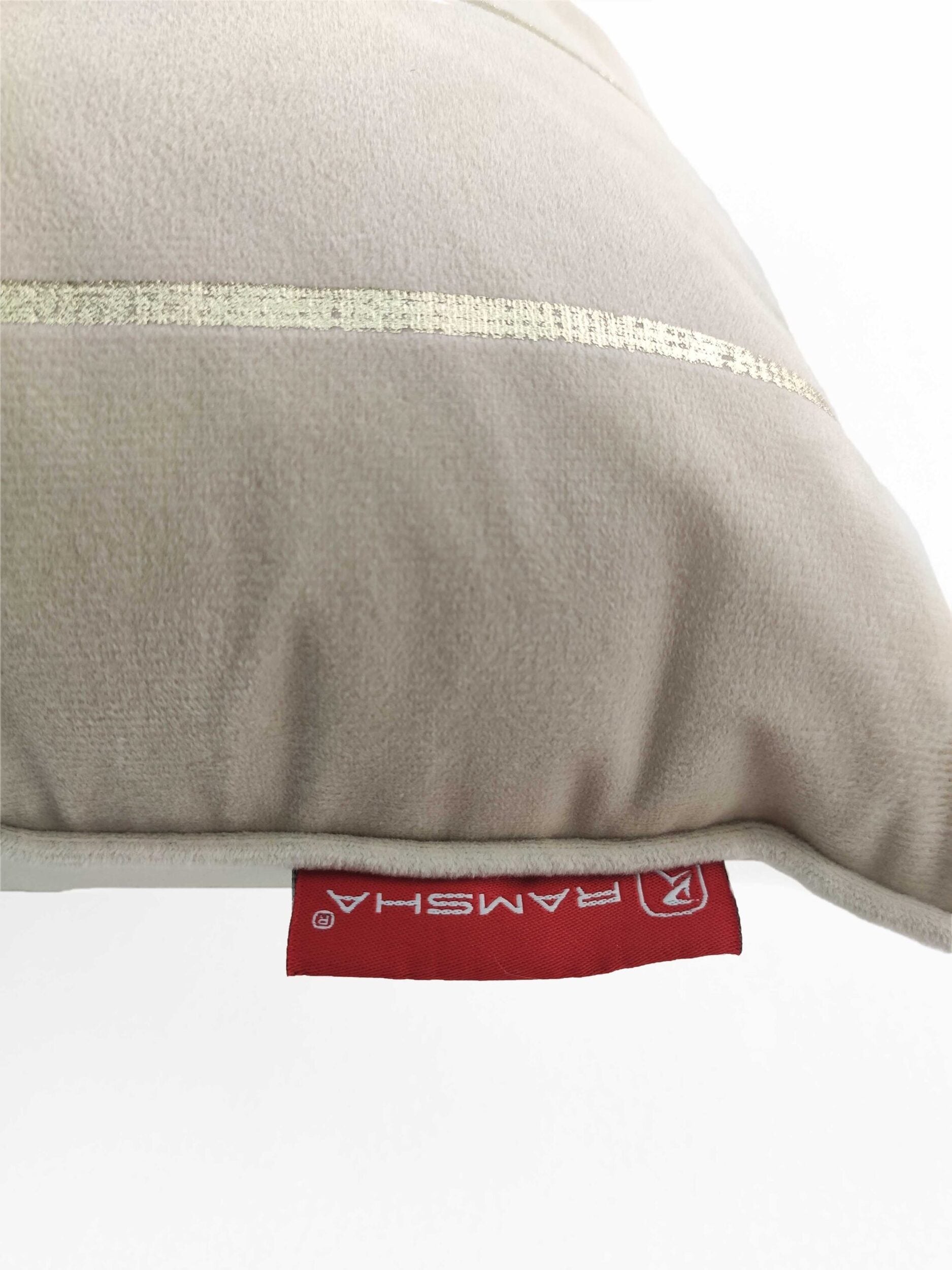A close-up of the 100% Polyester Cushion Cover CS-099 by RAMSHA HOME in wrinkle-resistant beige with a thin gold stripe and a red “RAMSHA” tag on the seam, displayed against a white background.