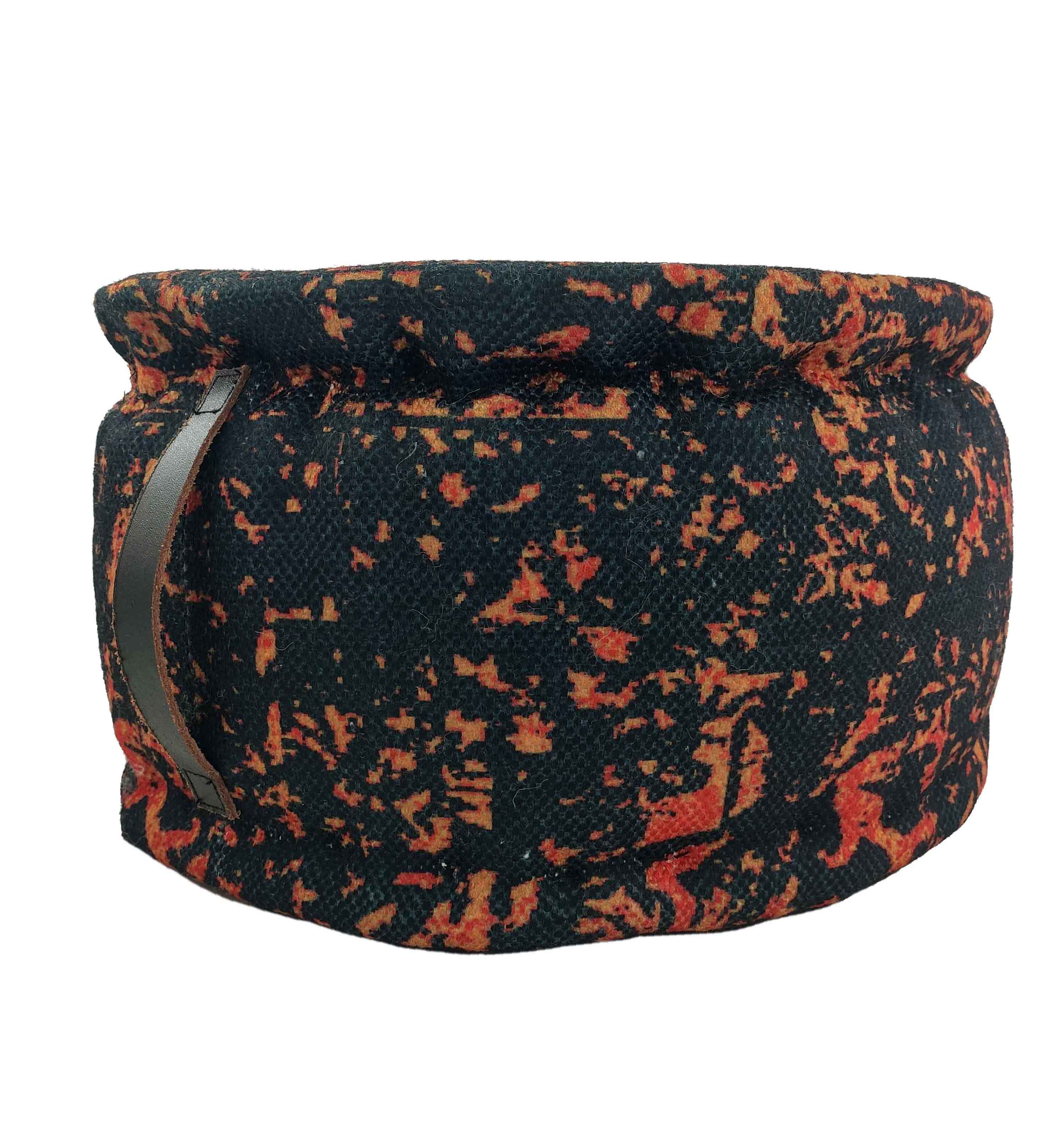 The RAMSHA HOME Printed Multi Color Pouf features a round fabric design with a mottled black, orange, and red pattern and a rolled rim. It has a leather handle on one side for easy carrying.