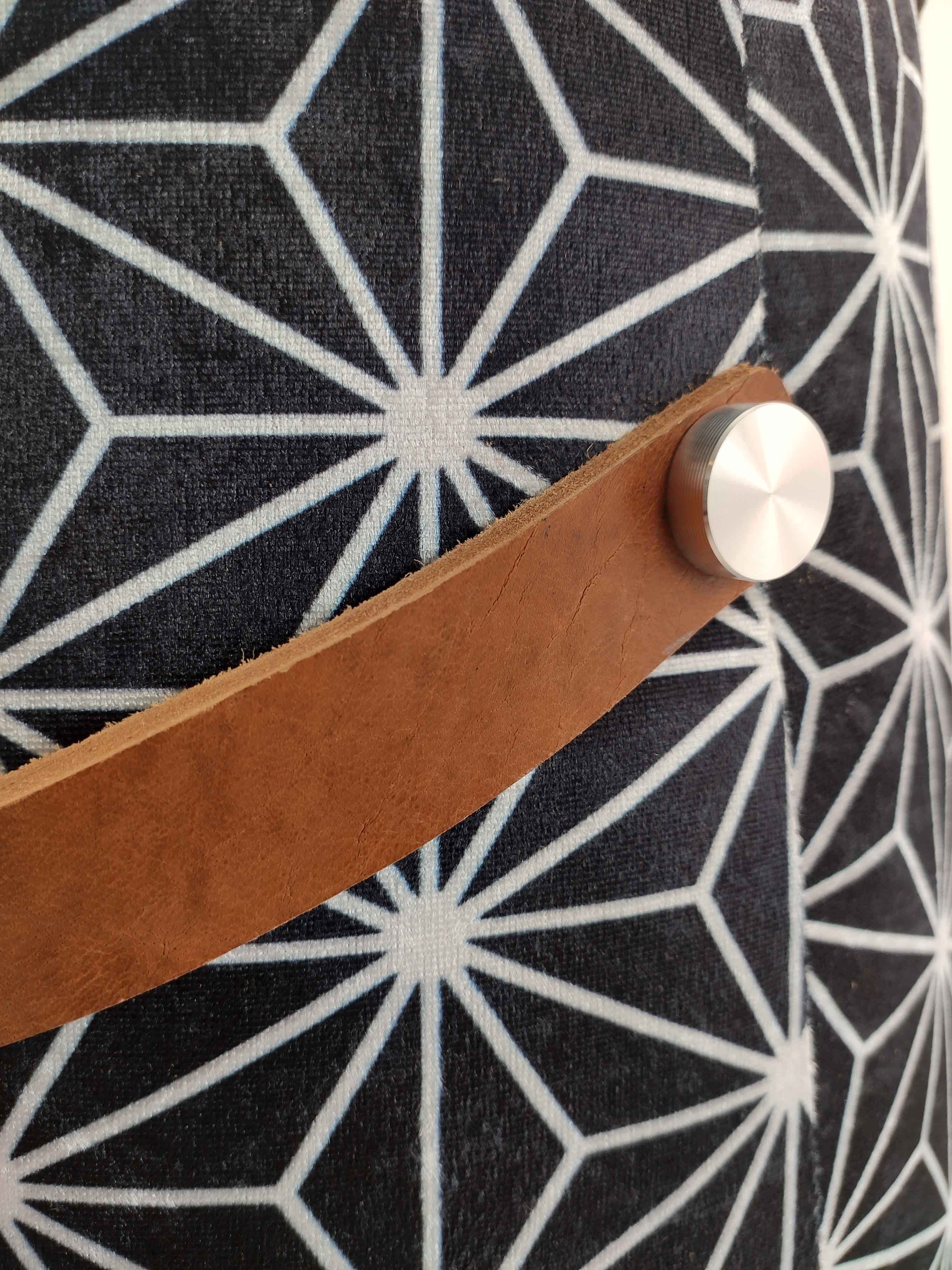 Close-up of RAMSHA HOME's Printed Pedestal Pouf With Leather Handle PF-027, featuring a geometric black and white pattern, brown leather handle, and silver button—an elegant addition to modern home décor.