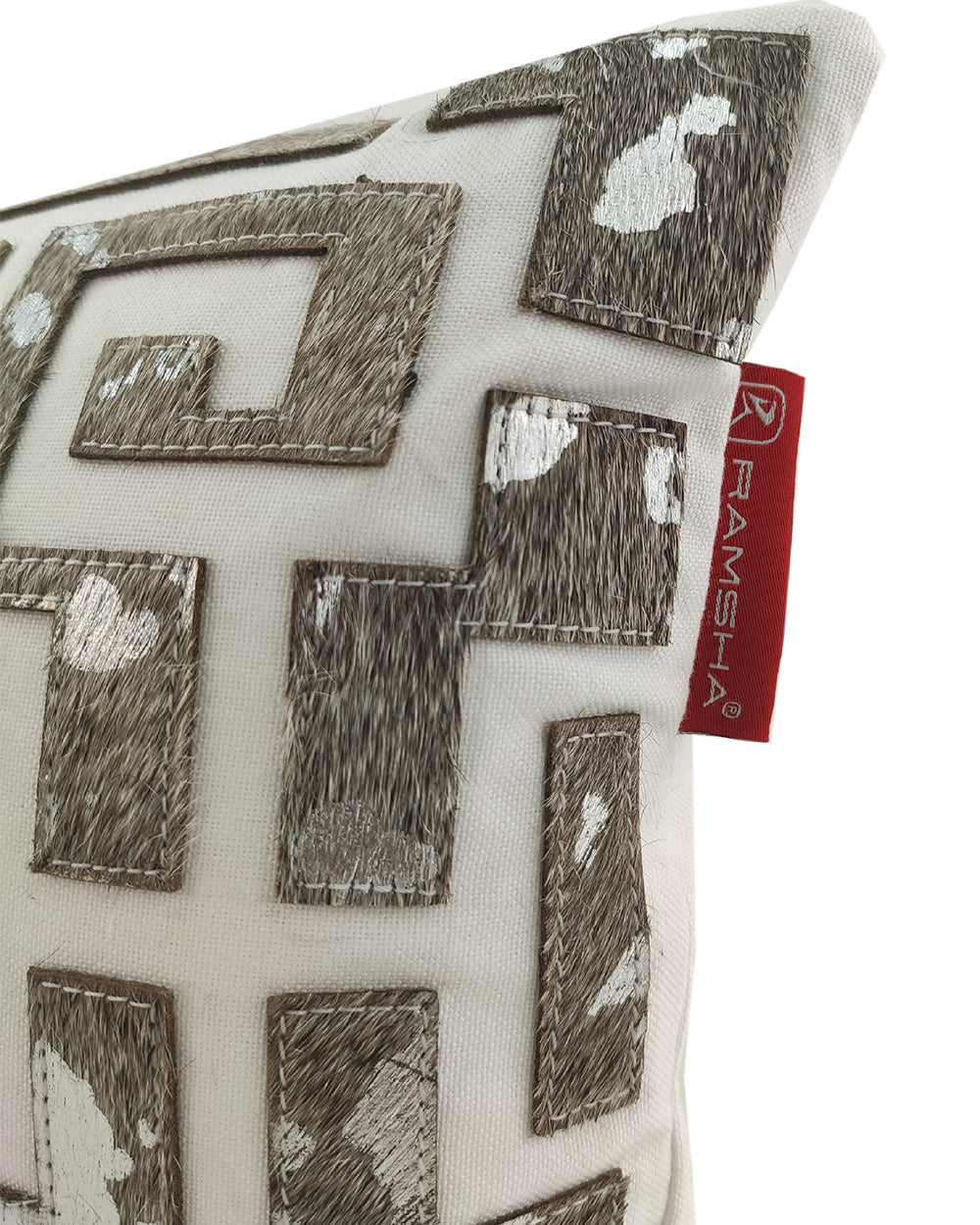 A close-up of the RAMSHA HOME Sofa & Chair Cushion CS-106, featuring a brown and white geometric cowhide pattern on cream, with a red RAMSHA HOME tag on the edge.