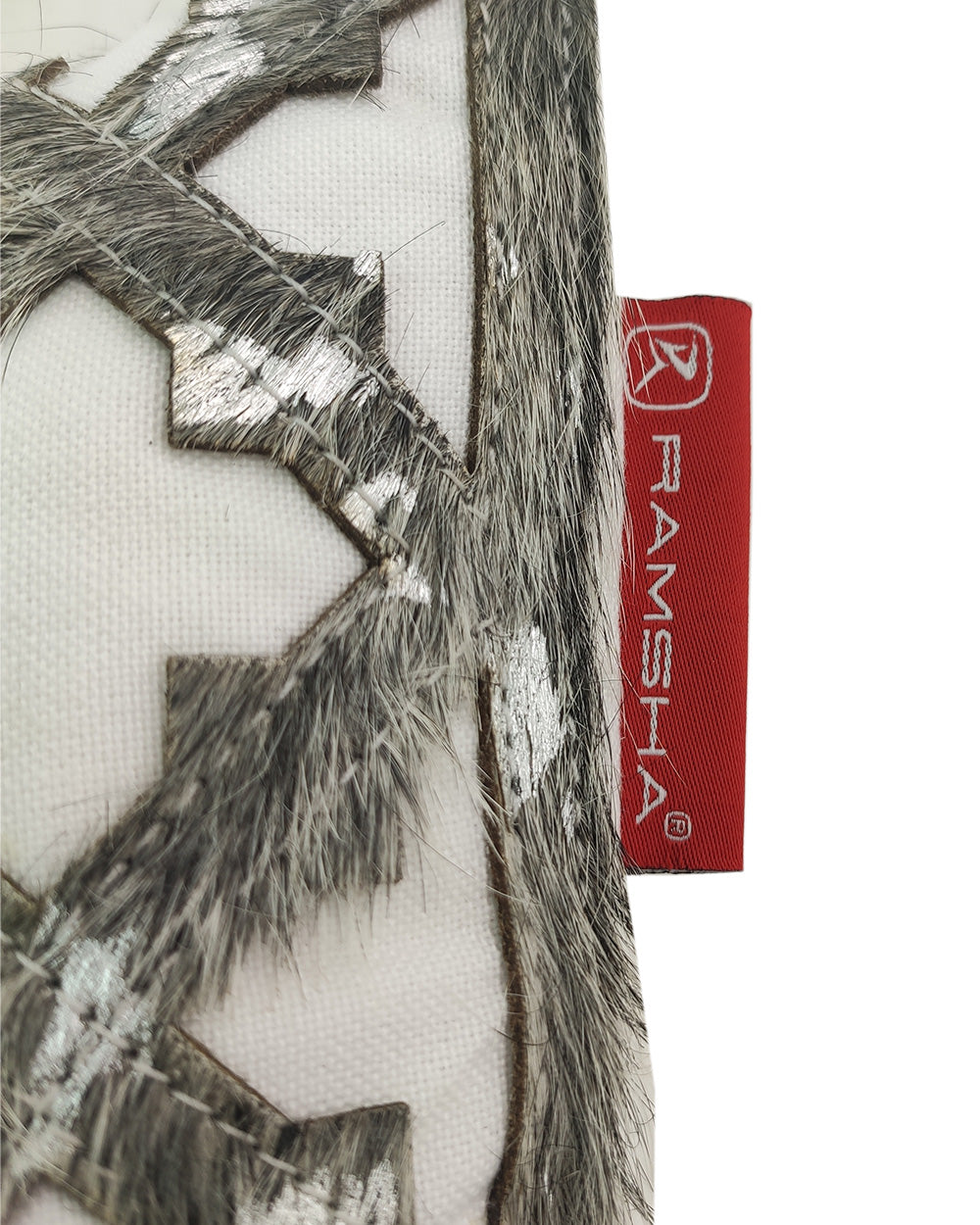 Close-up of the Home decor Leather Cushion CS-103 by RAMSHA HOME, featuring a silver and gray geometric pattern with faux fur texture. A red tag labeled RAMSHA adds a stylish accent to this elegant cushion, ideal for home decor.