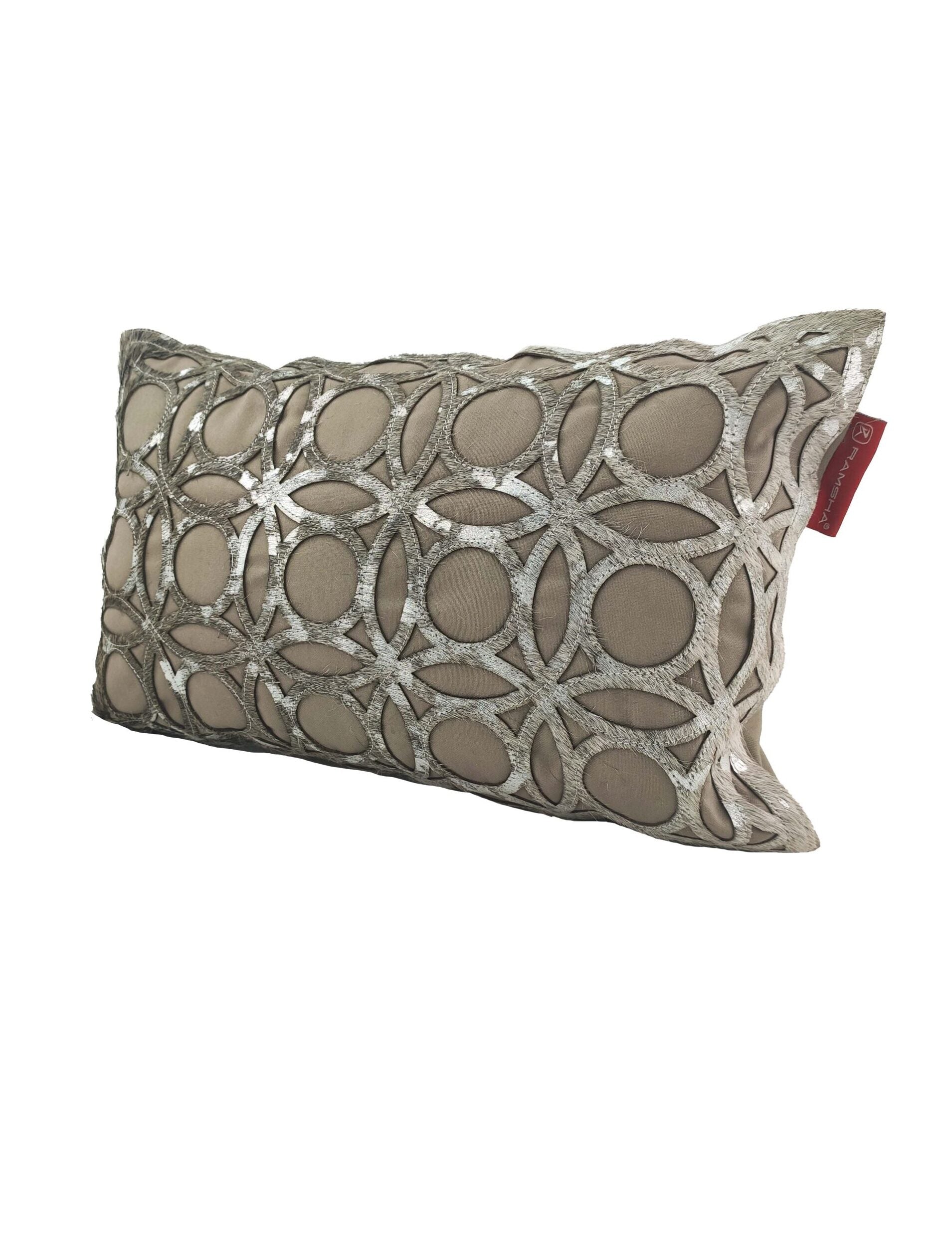 The RAMSHA HOME Leather Cushion CS-100 is a rectangular pillow with a beige base, metallic silver starburst embroidery, and a red side tag, offering high-quality support and an elegant textured look.
