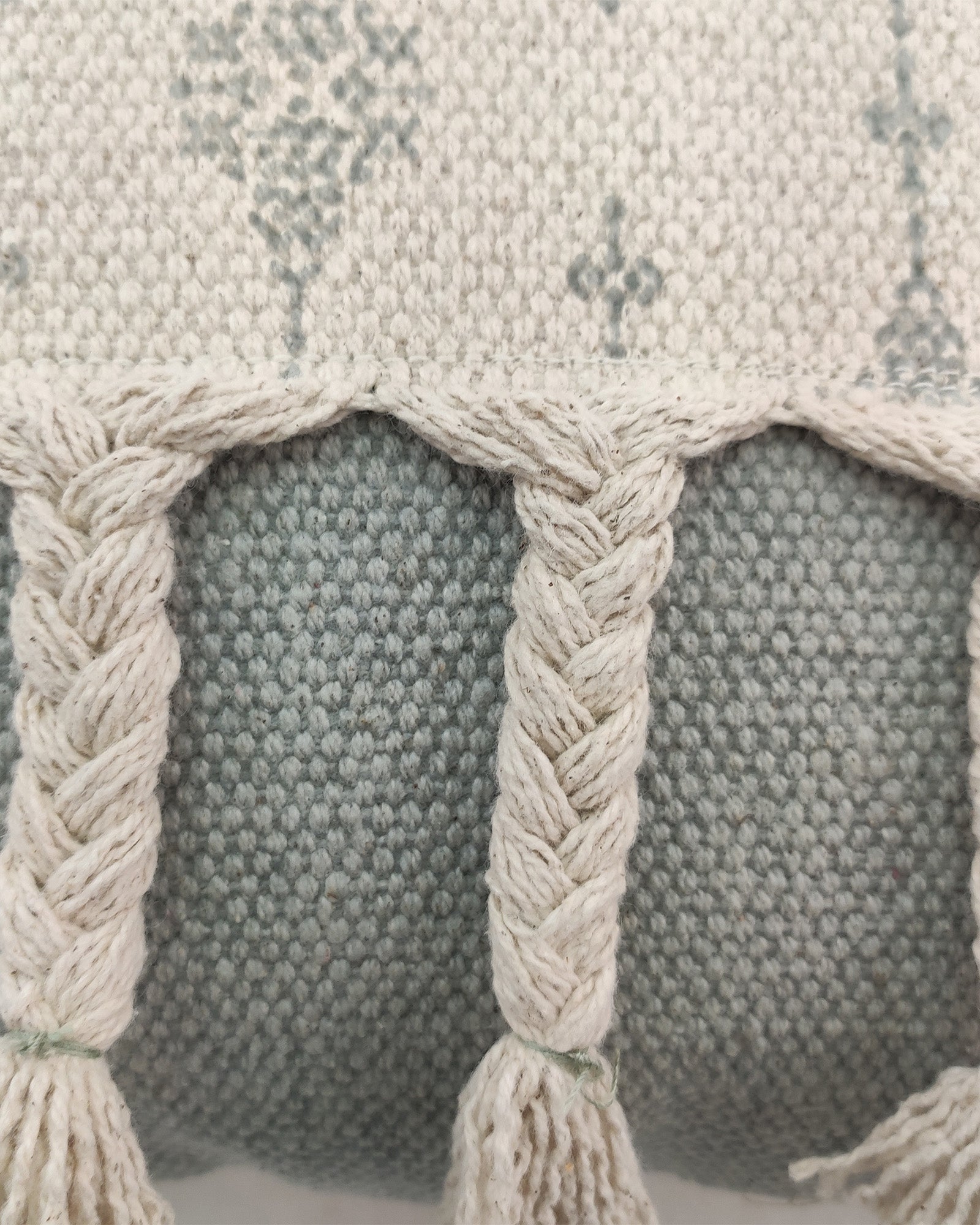Close-up of RAMSHA HOME’s Printed Cotton Cushion With Fringes cs-172, showing its thick, cozy textured fabric and braided off-white tassels over a light grayish-blue background—perfect for adding style and comfort to any space.