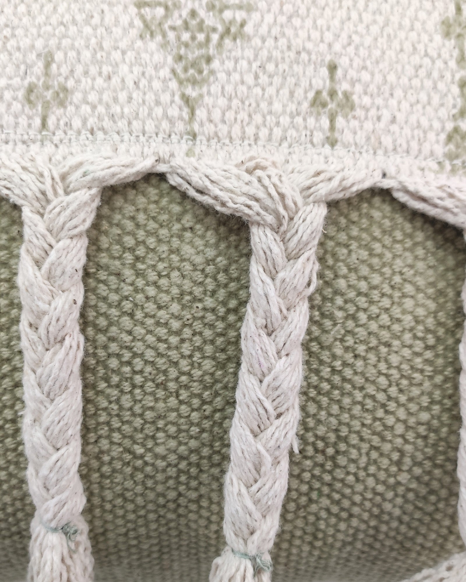 Close-up of the RAMSHA HOME Printed Cotton Cushion With Fringes cs-172, showcasing sage green woven fabric, vertical white braided cords, and a patterned border for decorative flair.