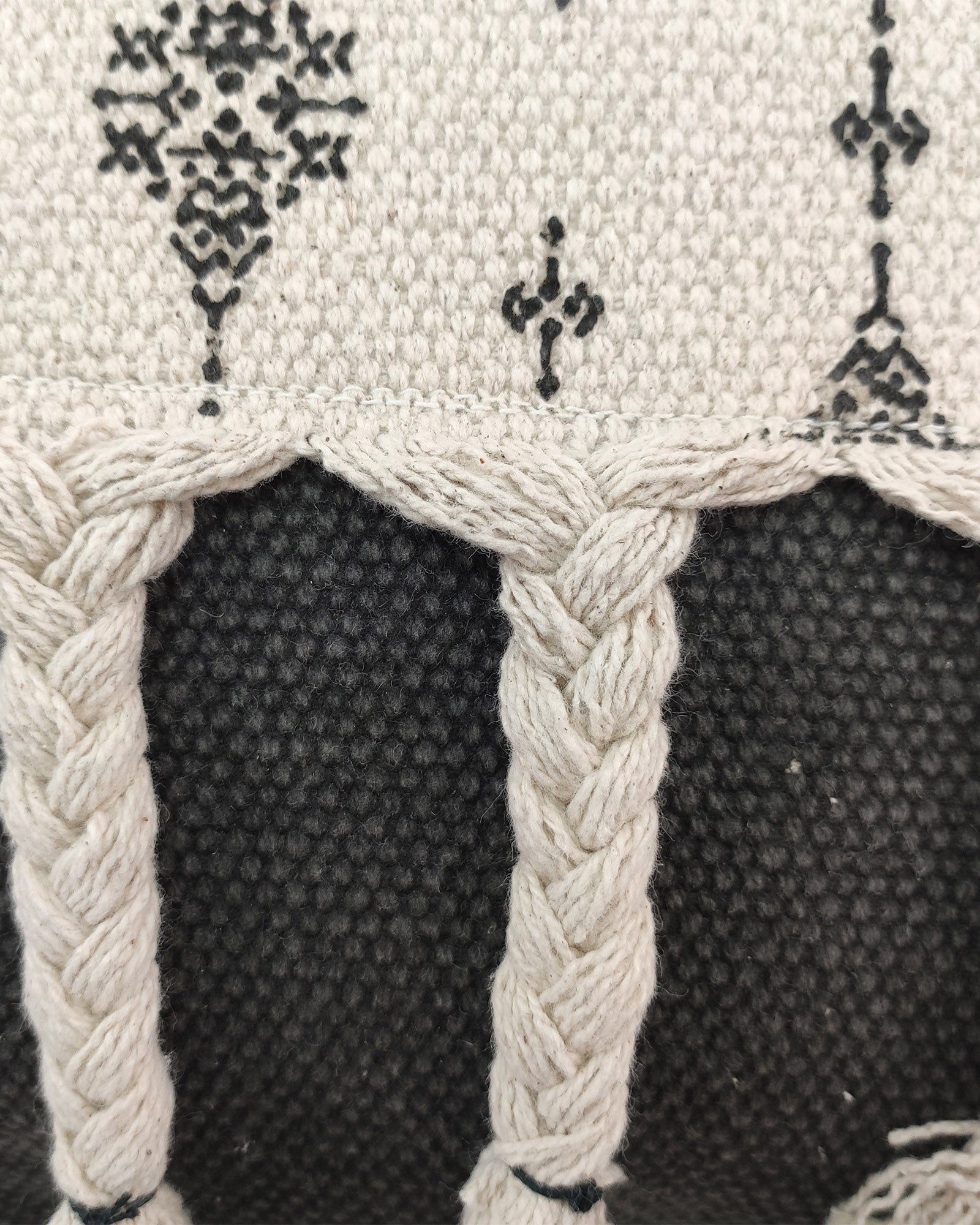 Close-up of RAMSHA HOME's Printed Cotton Cushion With Fringes cs-172, featuring a black and white geometric print on cotton. The design includes black motifs on white at the top and thick braided white threads over textured black below.