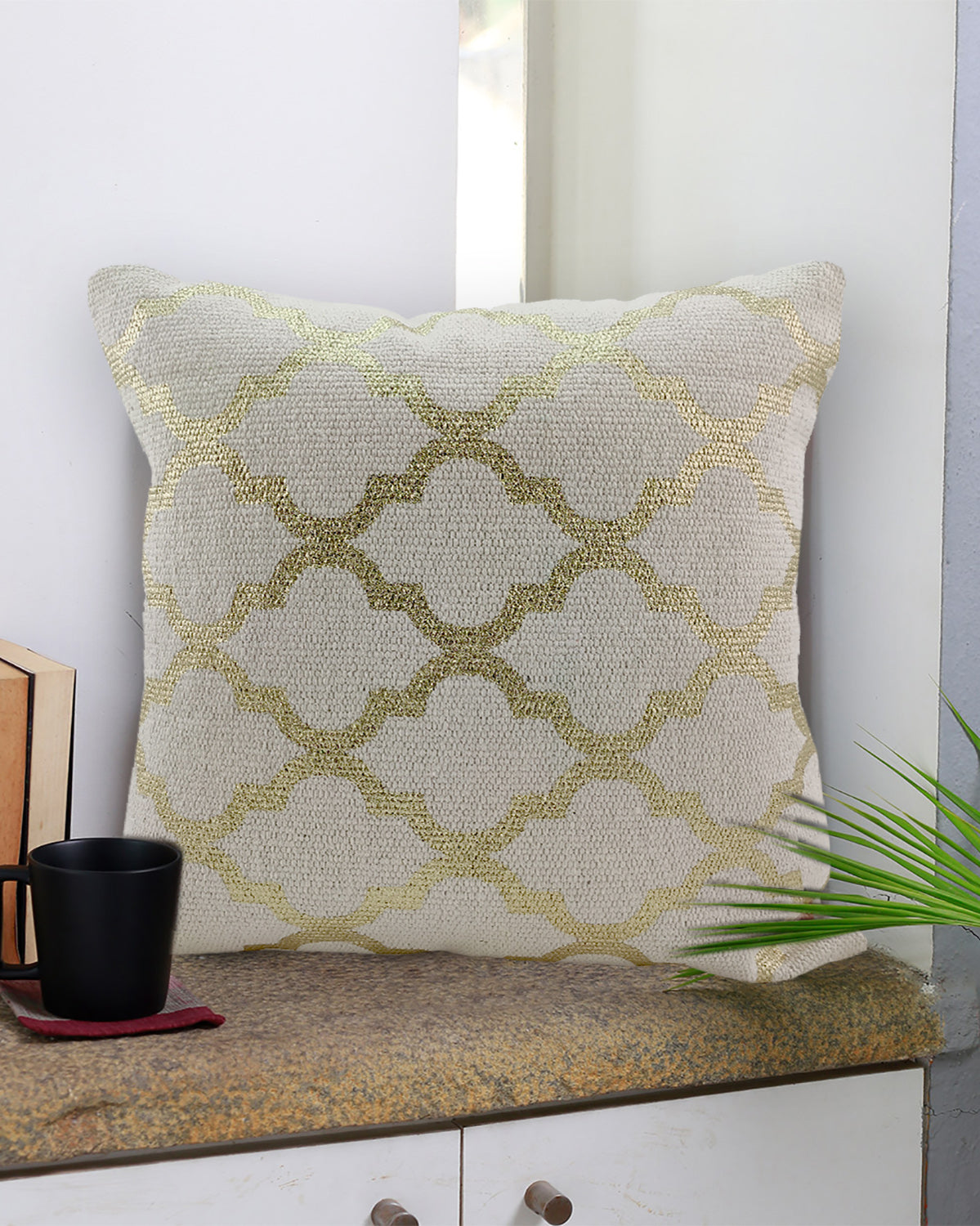 The RAMSHA HOME Cotton Cushion With Gold Foil Print CS-178 sits on a stone countertop beside a black coffee mug, wooden decor, and green plant, with white walls and a window in the background.