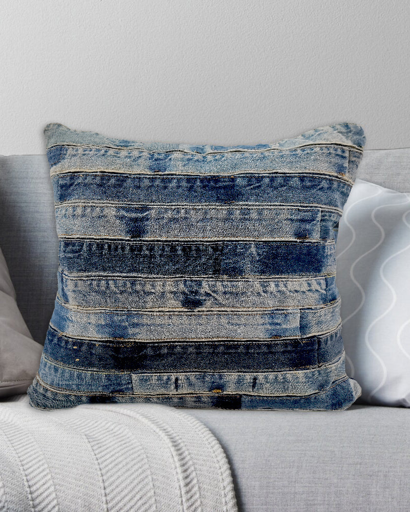 The RAMSHA HOME Denim Cotton Cushion With Polyfill cs-188, crafted from denim fabric strips, rests on a light gray sofa with white and gray pillows and a textured white blanket, adding comfort and style to your living space.