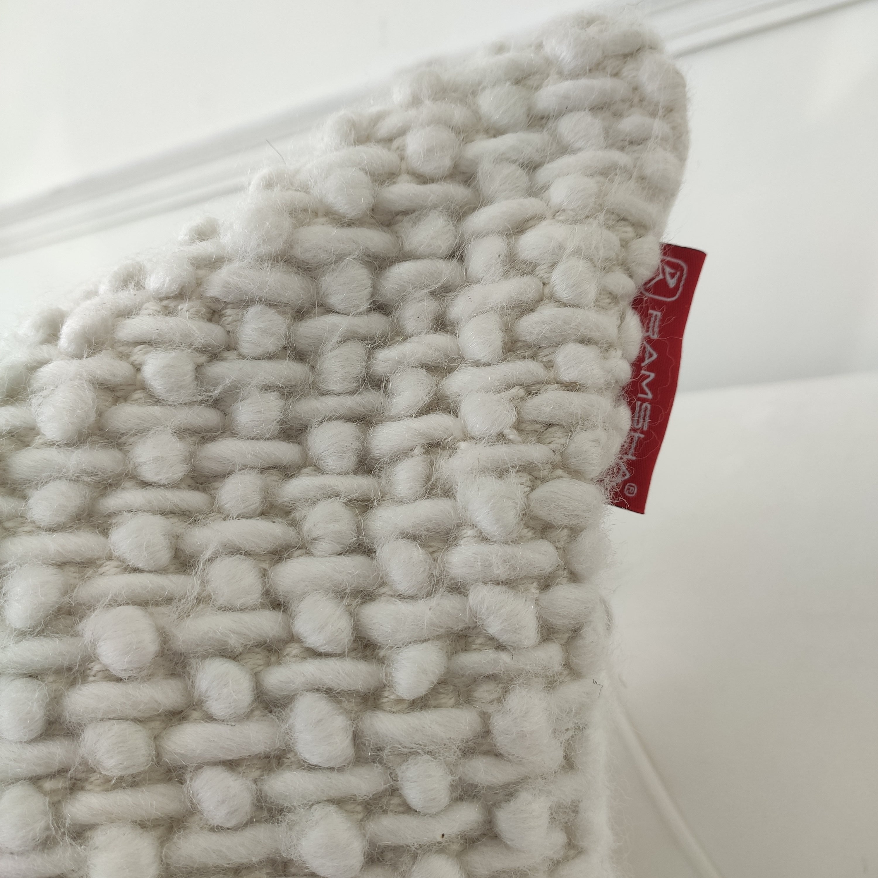 Close-up of the RAMSHA HOME Woven Cushion Soft Sofa Cushion CS-279 showing chunky off-white yarn and a small red fabric tag on the side, set against a soft white background, evoking comfort and style.