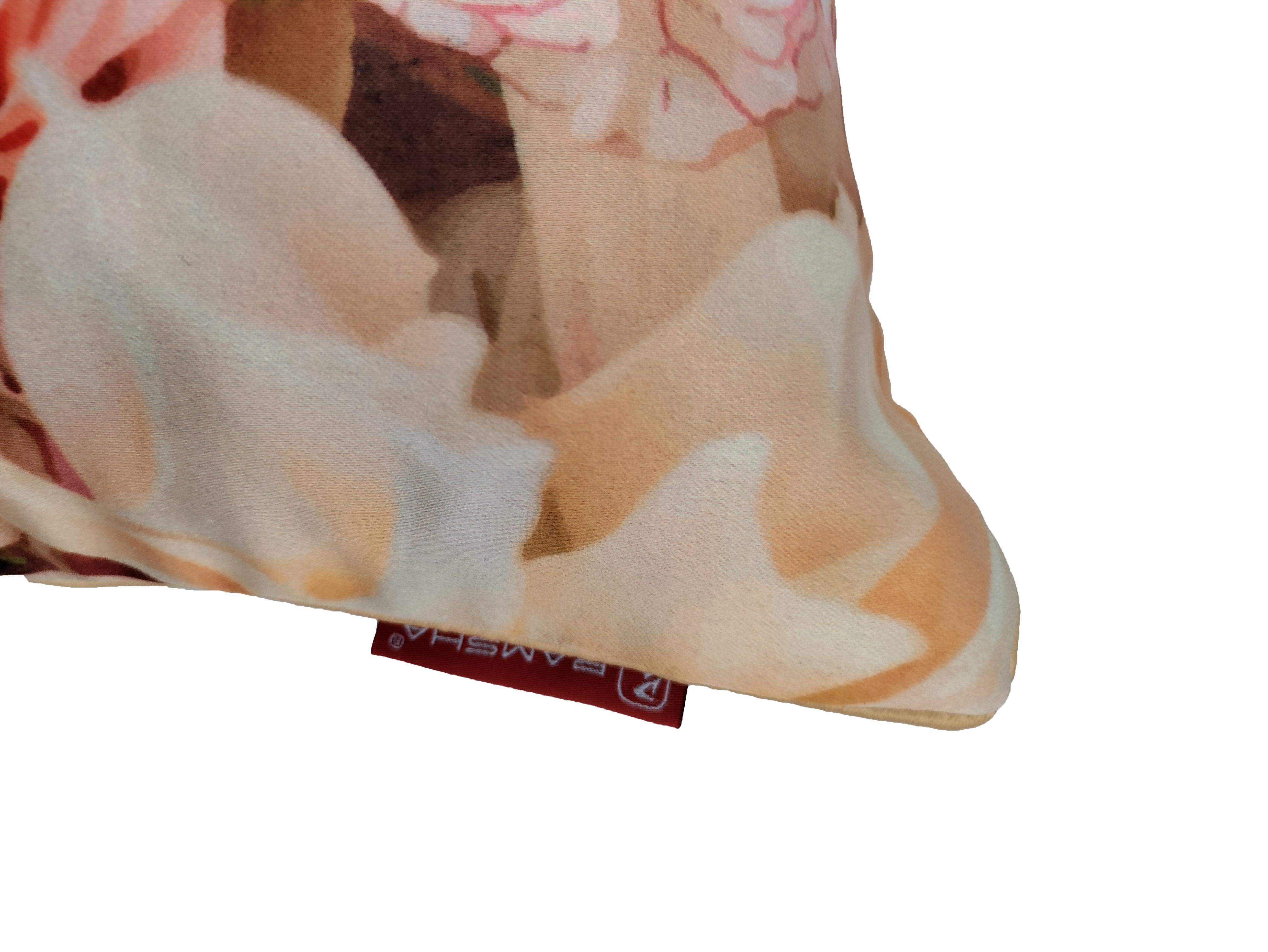 A close-up of the RAMSHA HOME Floral Printed Multi Color Cushion, showcasing pink and beige patterns and a red fabric tag with white text on the bottom edge—an elegant decor piece set against a white background.