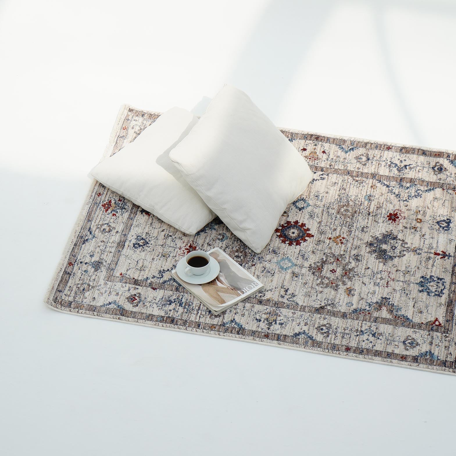 Two white pillows rest on the Cream Color Indoor Area Rug K655I by RAMSHA HOME, next to a tray with coffee and snacks, all atop a bright white floor.