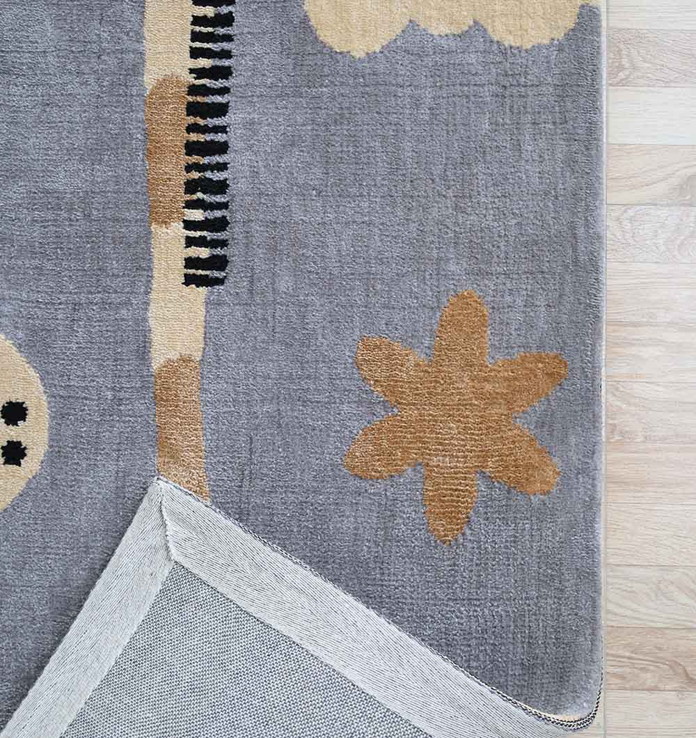 The RAMSHA HOME Giraffe Nursery Rug - Blue Grey Cloud (120x180cm) lies on a light wood floor, its abstract shapes and star-like figure visible. One corner is flipped to display the textured, light-colored underside.