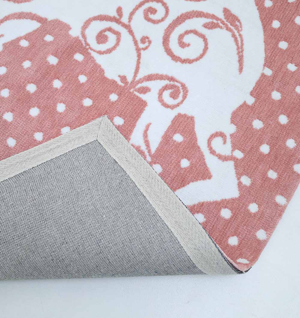 A close-up of the RAMSHA HOME Unicorn Kids Rug - Pink Fantasy Playroom Area Carpet KD 004 (120X180 cm) shows pink and white cartoon patterns with polka dots, a corner flipped to reveal the plain gray underside and stitched edging.