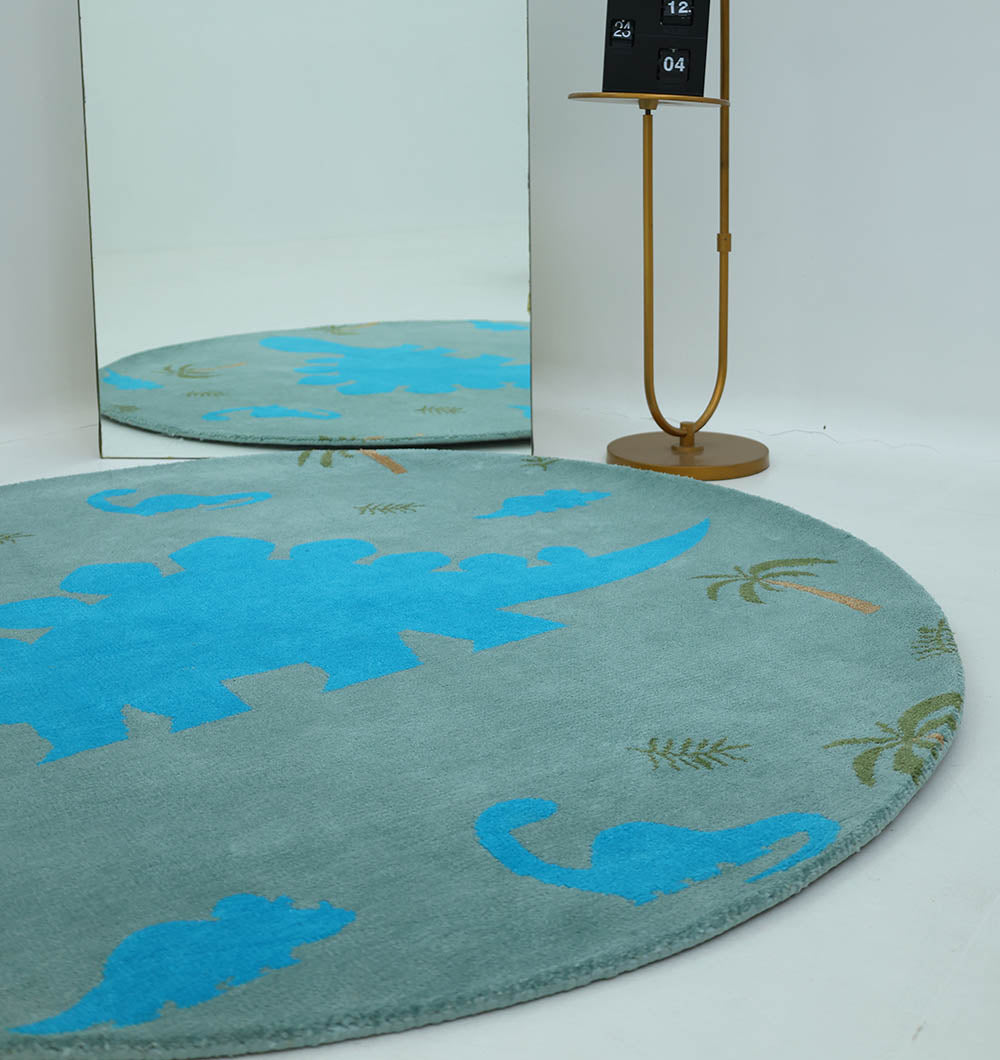 The RAMSHA HOME Kids Dinosaur Rug - Blue & Green (KD 008, 150 cm) brightens the playroom with blue dinos and green palm trees. It sits in front of a standing mirror, paired with a gold floor lamp with a black shade on the white floor.