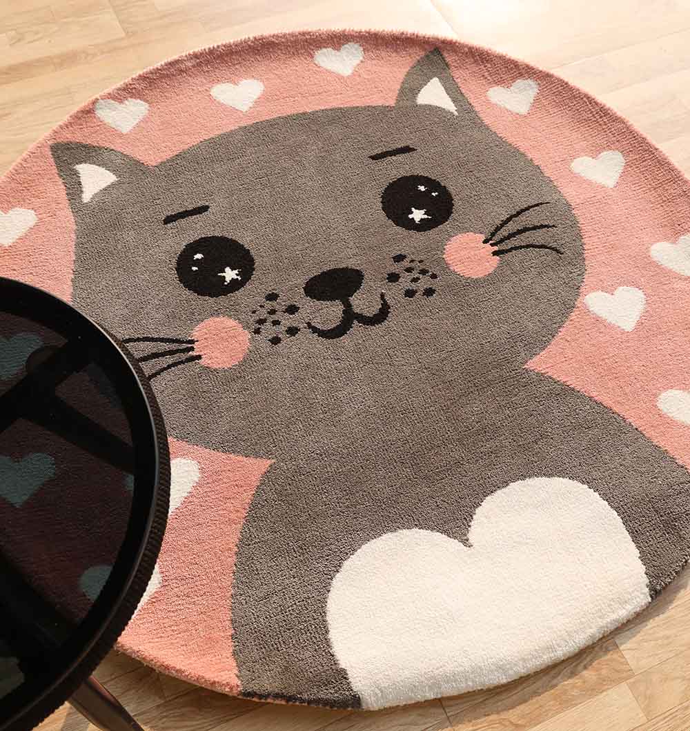 The RAMSHA HOME Kids Cat Rug - Pink & Grey (KD 009, 120 cm) features a cute cartoon cat face with big eyes and a white heart on its chest, set on a pink background with white hearts—perfect for any playroom or nursery.