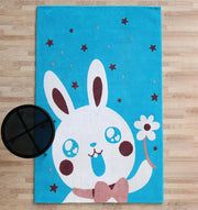 The RAMSHA HOME Multi Color Kids Area Carpet - KD 011 (120x180 cm) features a turquoise bunny rug with a large cartoon white rabbit, red stars, and a round black table on a light wooden floor—perfect kid-friendly decor.